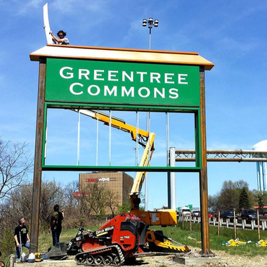 Sign for Greentree Commons being worked on by a construction crew. A lift is used to help with the work.