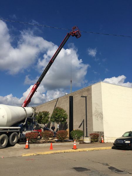 Concrete truck and tall crane next to building on a sunny day with blue sky.