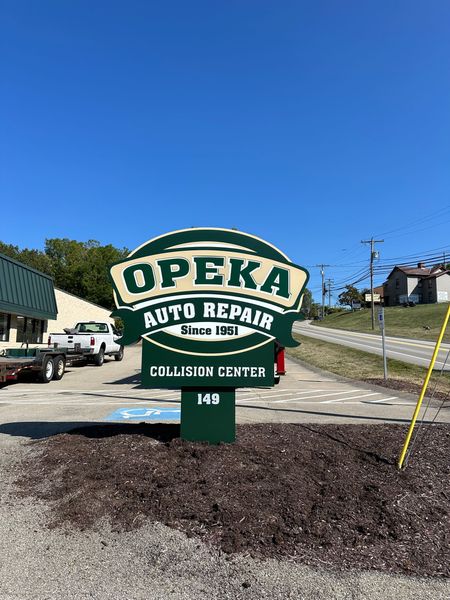 Sign for OPEKA Auto Repair, a collision center, on a sunny day.
