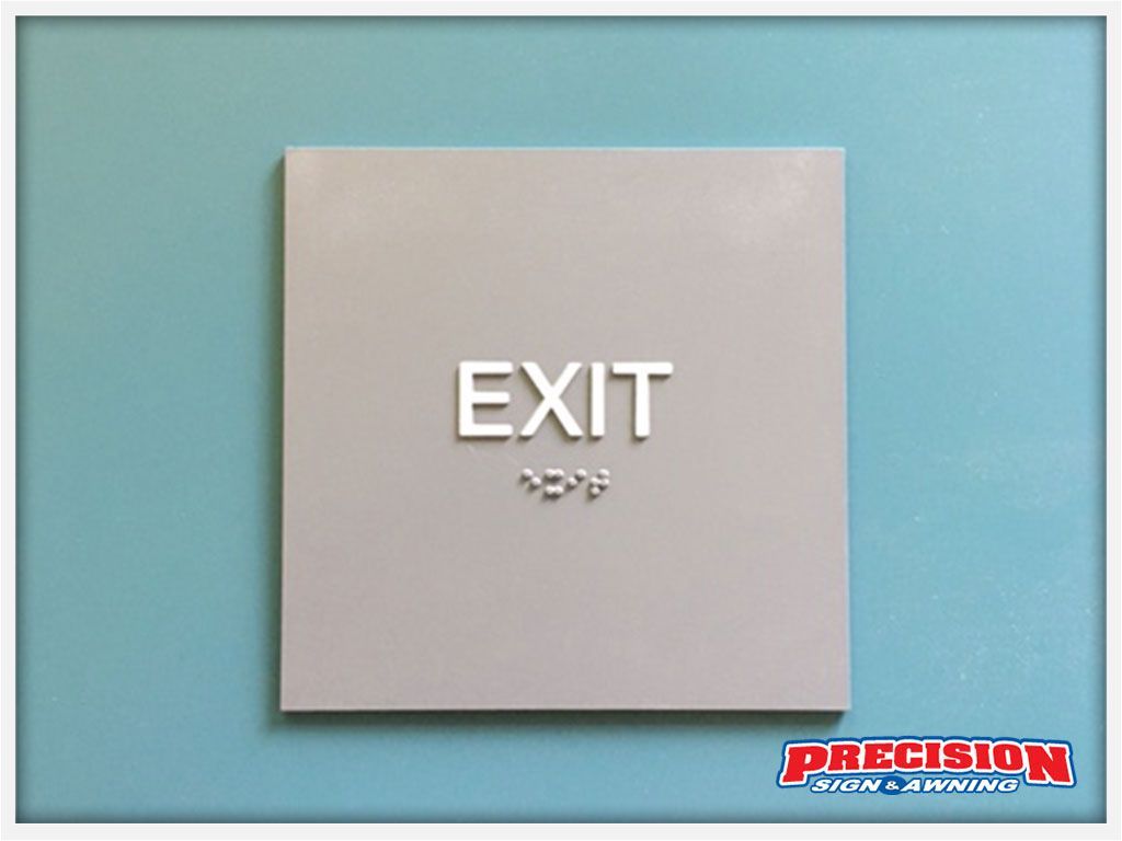 Gray "EXIT" sign with braille on a teal wall.