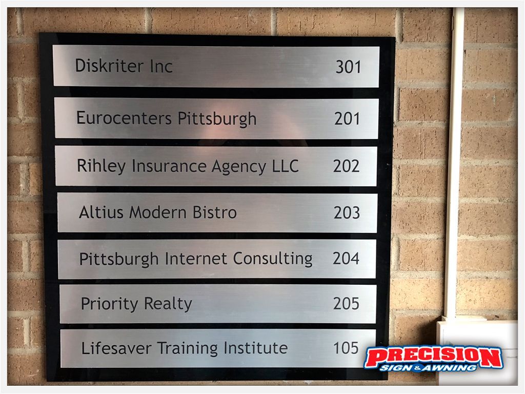 Directory sign with company names and room numbers on a brick wall.