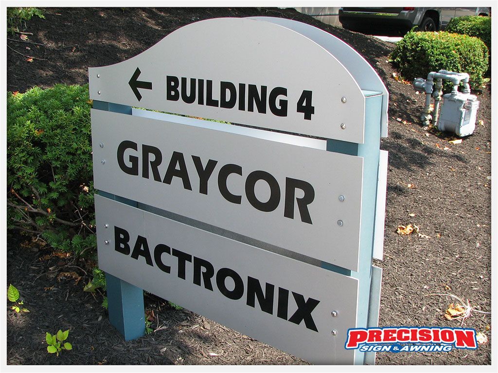 Signpost for Building 4, Graycor, and Bactronix; gray with black text and blue posts.
