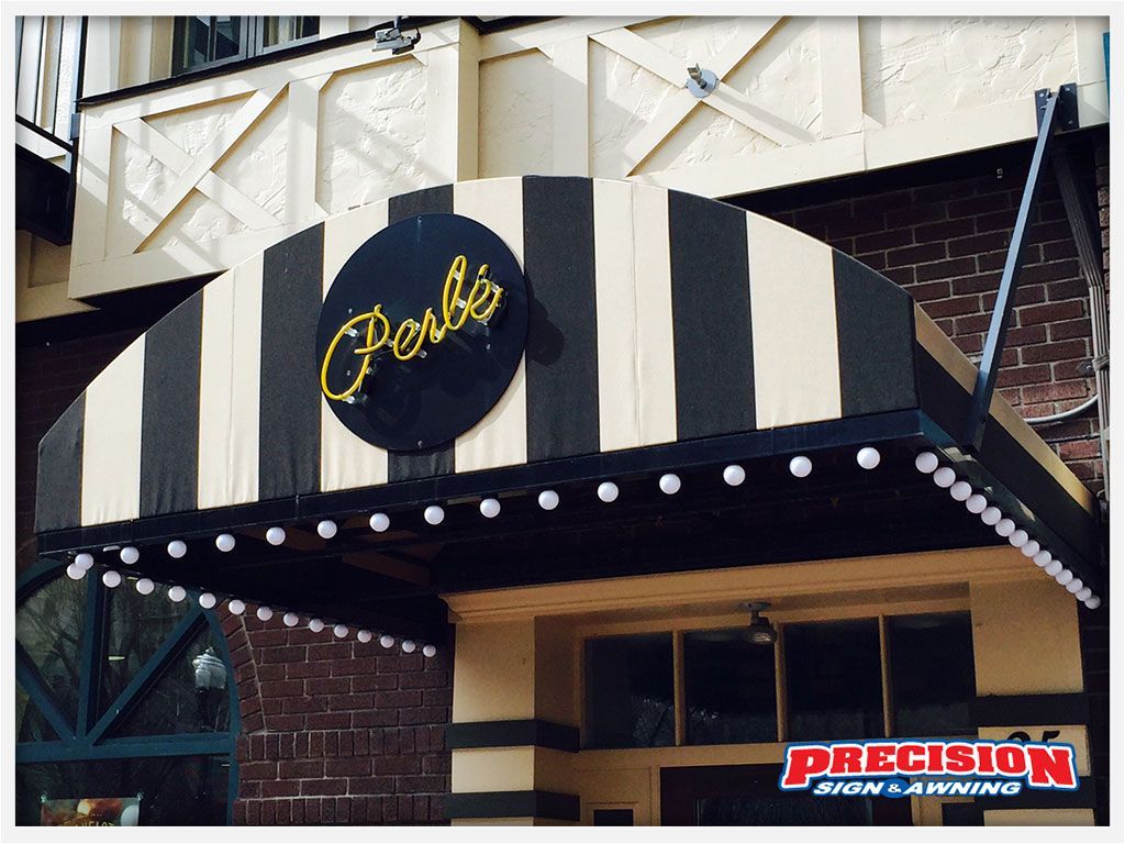 Black and beige striped awning over Perbi's restaurant entrance; neon sign, brick building, string lights.