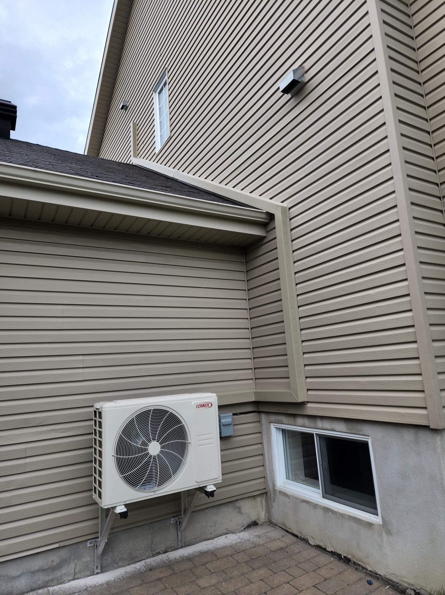 Unité de climatisation fixée sur un mur de bardage beige d'une maison.