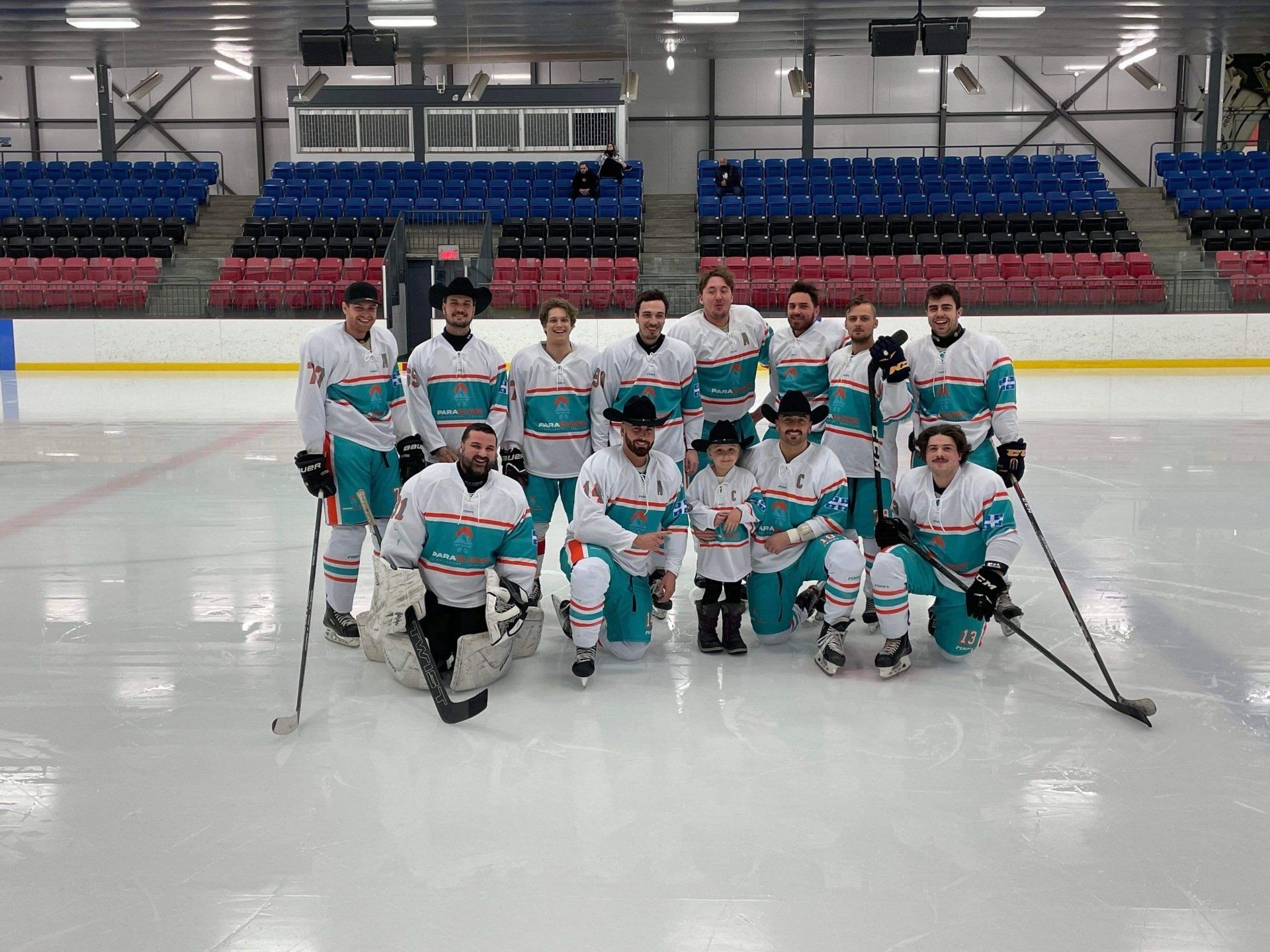 Une équipe de hockey pose sur la patinoire, vêtue de maillots turquoise et blancs. Certains portent des chapeaux de cow-boy.
