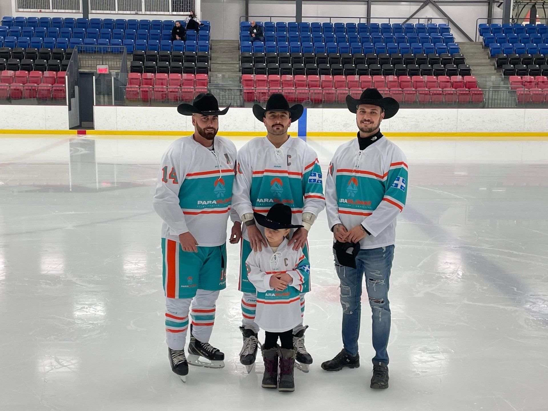 Quatre personnes sur une patinoire, trois en maillots de hockey et chapeaux de cow-boy avec un enfant. On aperçoit les gradins de l'aréna en arrière-plan.