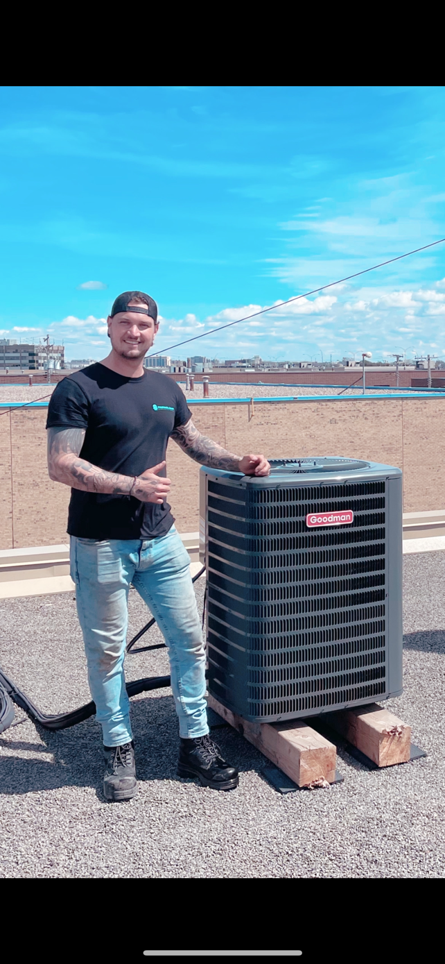 Un homme se tient debout à côté d'un climatiseur sur un toit, sous un ciel bleu.