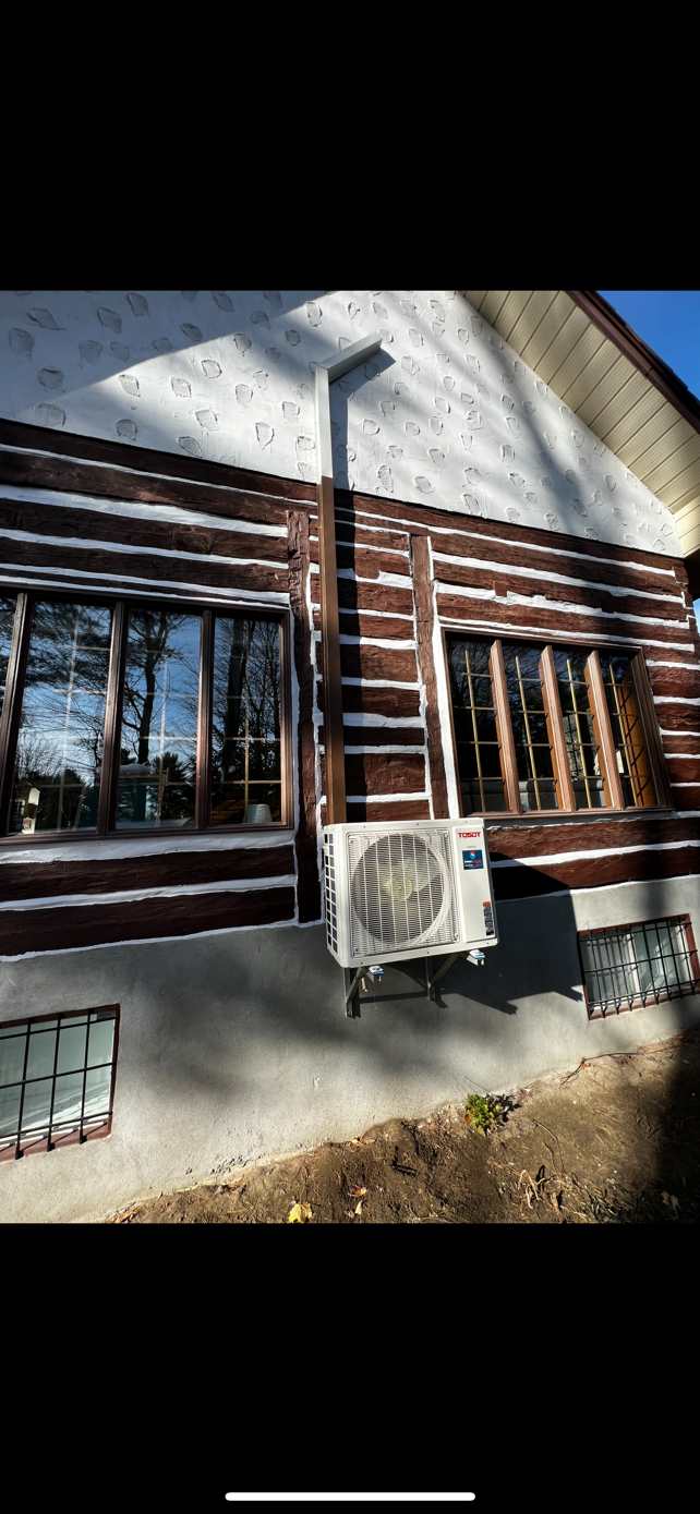 Un chalet en rondins bruns avec de grandes fenêtres et un climatiseur mural.