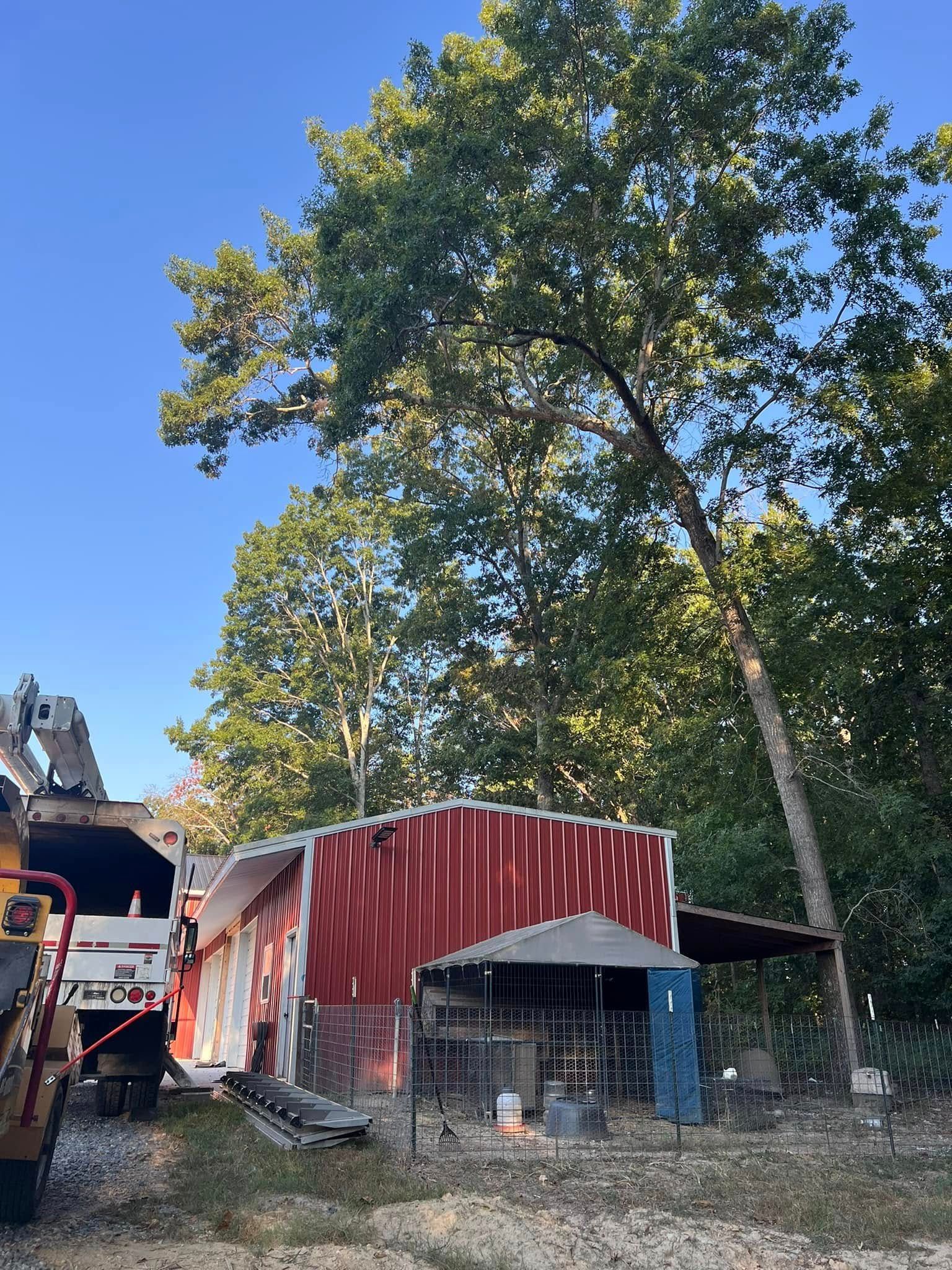 A large utility truck parked next to a red barn-style building with a green roof, set against a backdrop of tall trees.