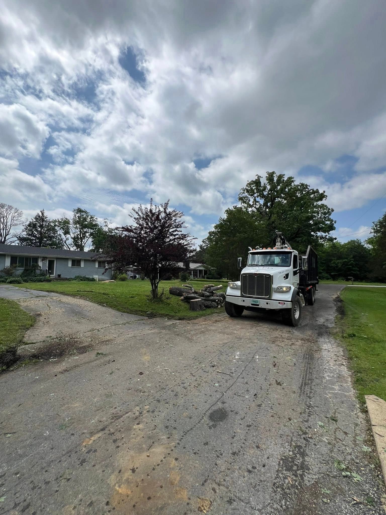 A white dump truck parked on a gravel driveway near a house under a cloudy blue sky.