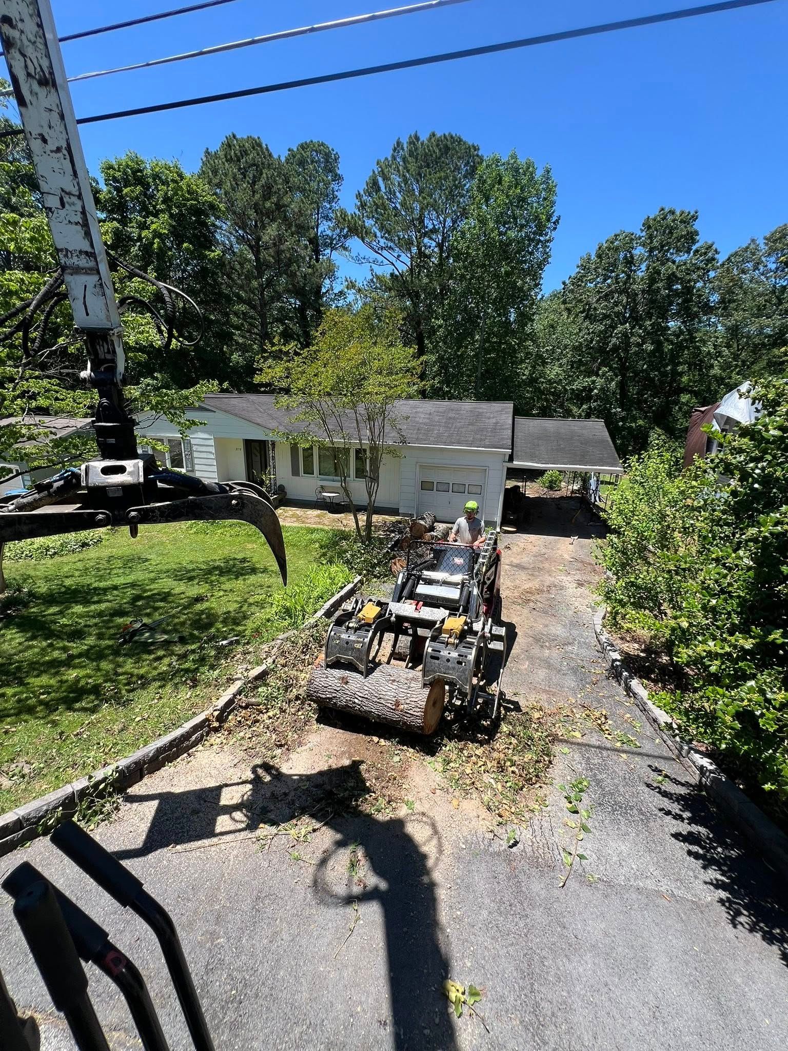 A tree removal crew uses a crane and specialized equipment to move large log sections on a residential driveway.