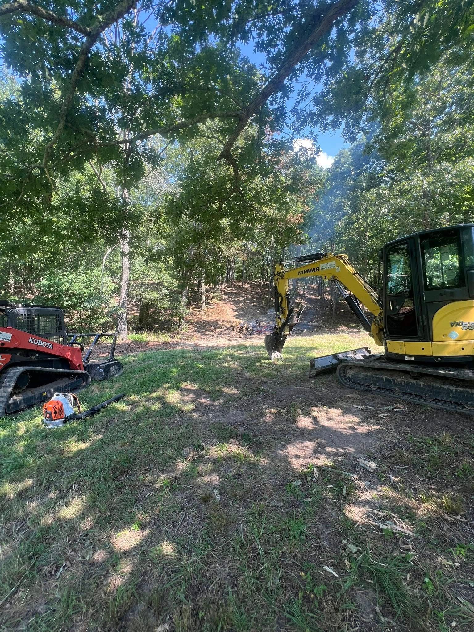 A red track loader and a yellow excavator parked in a sunny, wooded clearing with scattered debris.