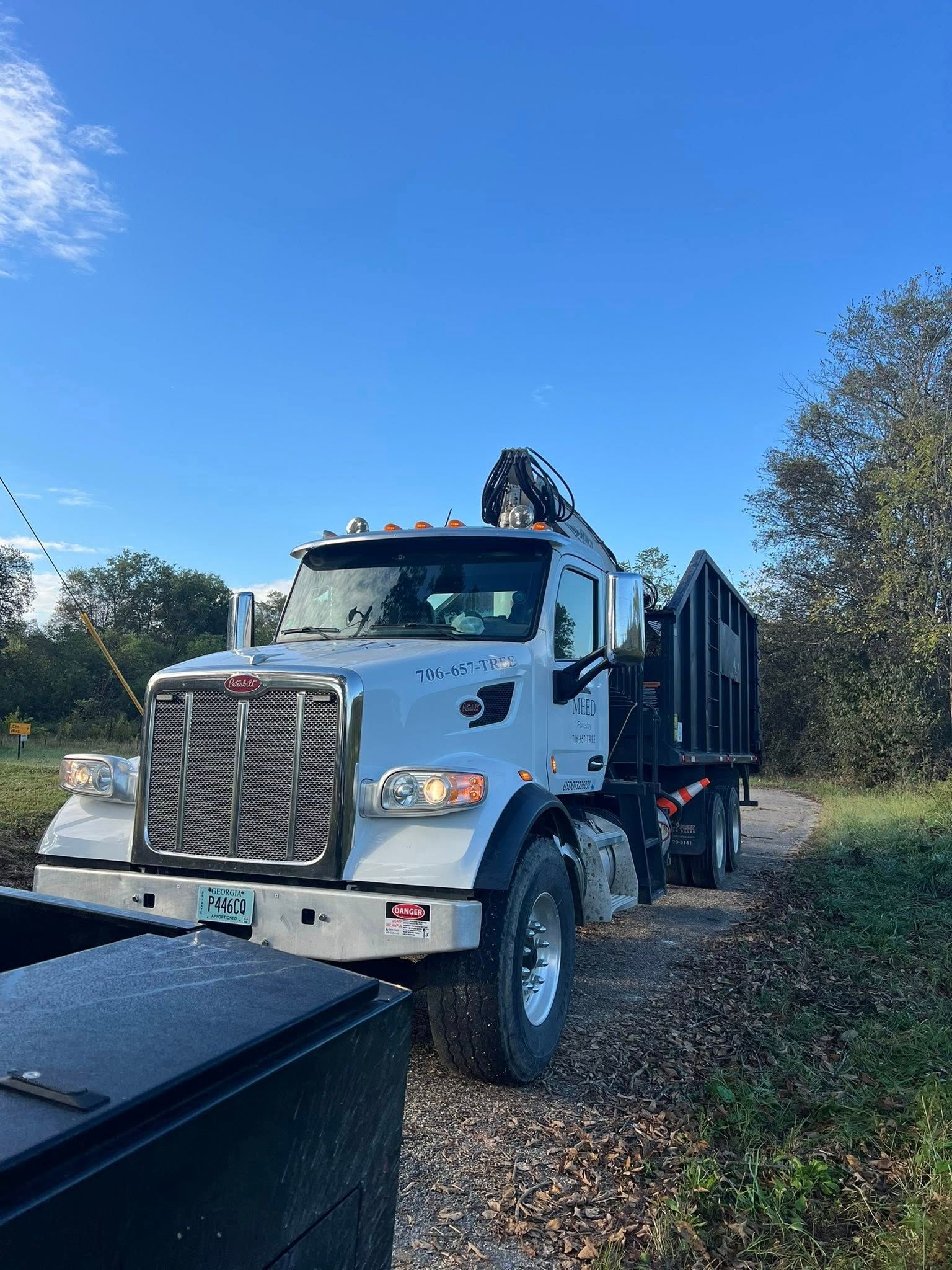 A white Peterbilt dump truck with a hydraulic crane parked on a gravel path against a clear blue sky.