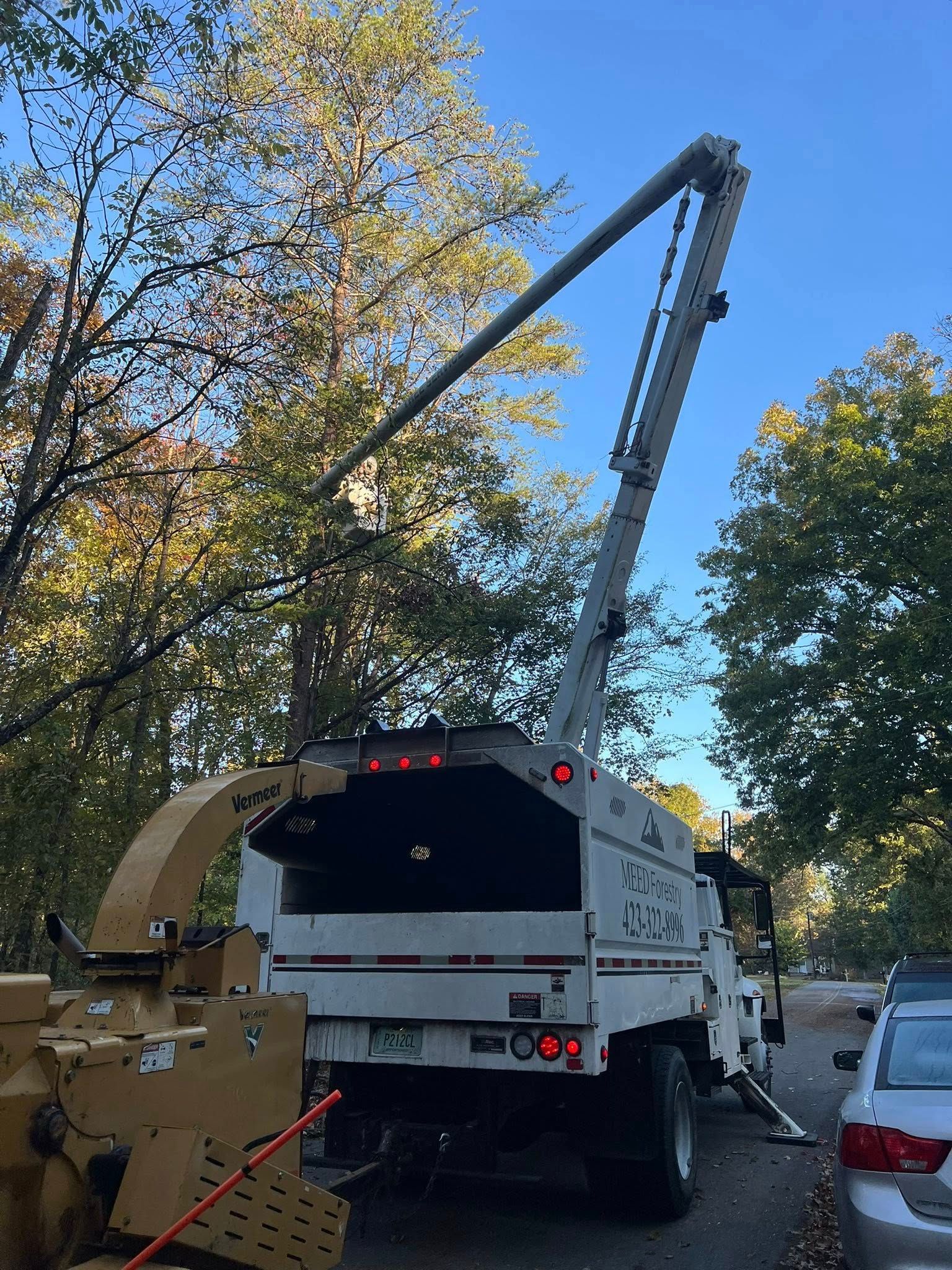 A tree service truck with an extended boom and an attached wood chipper parked on a residential street.