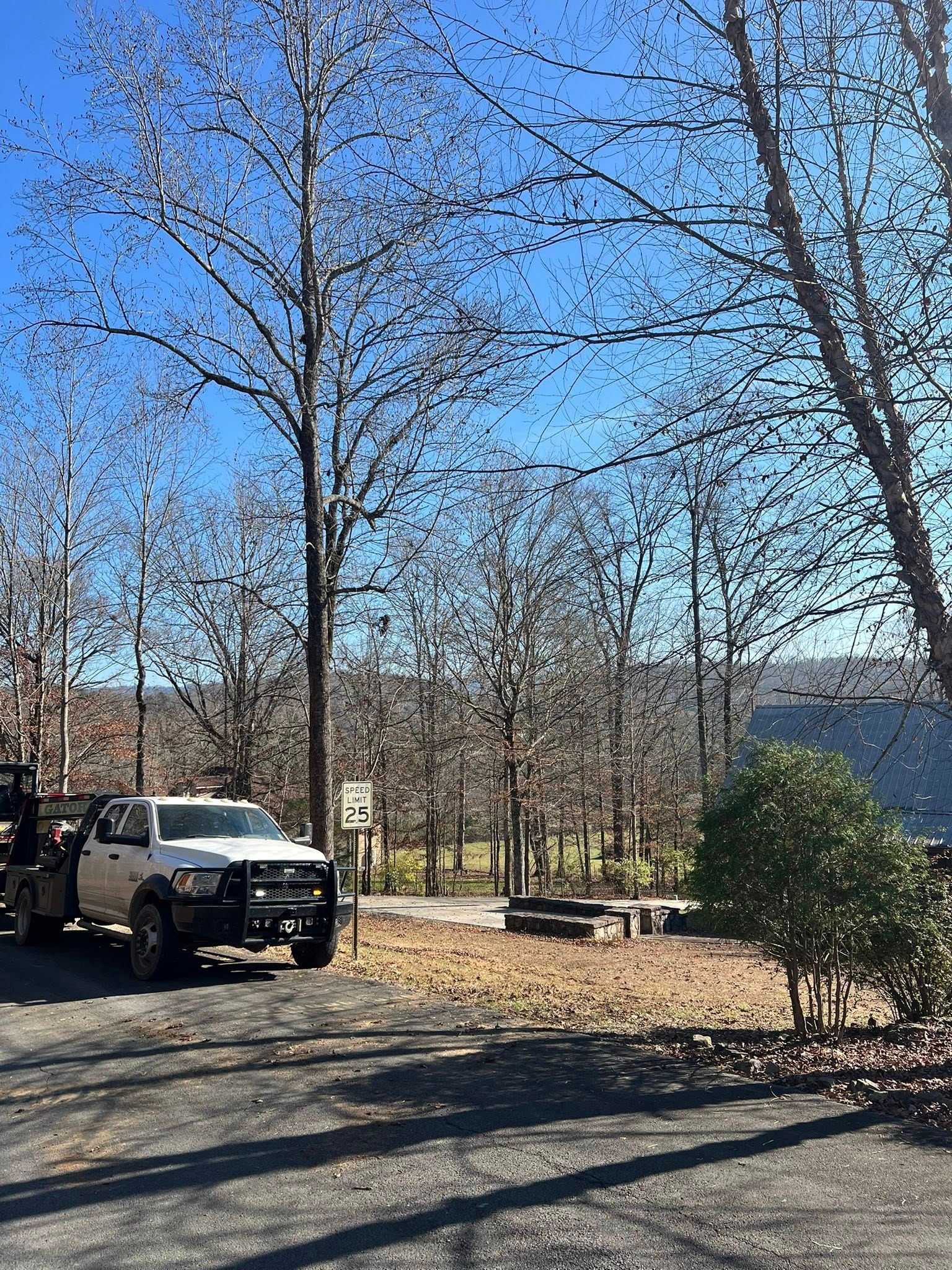 A white utility truck parked on a gravel drive in a wooded, sunny outdoor setting with a clear blue sky.