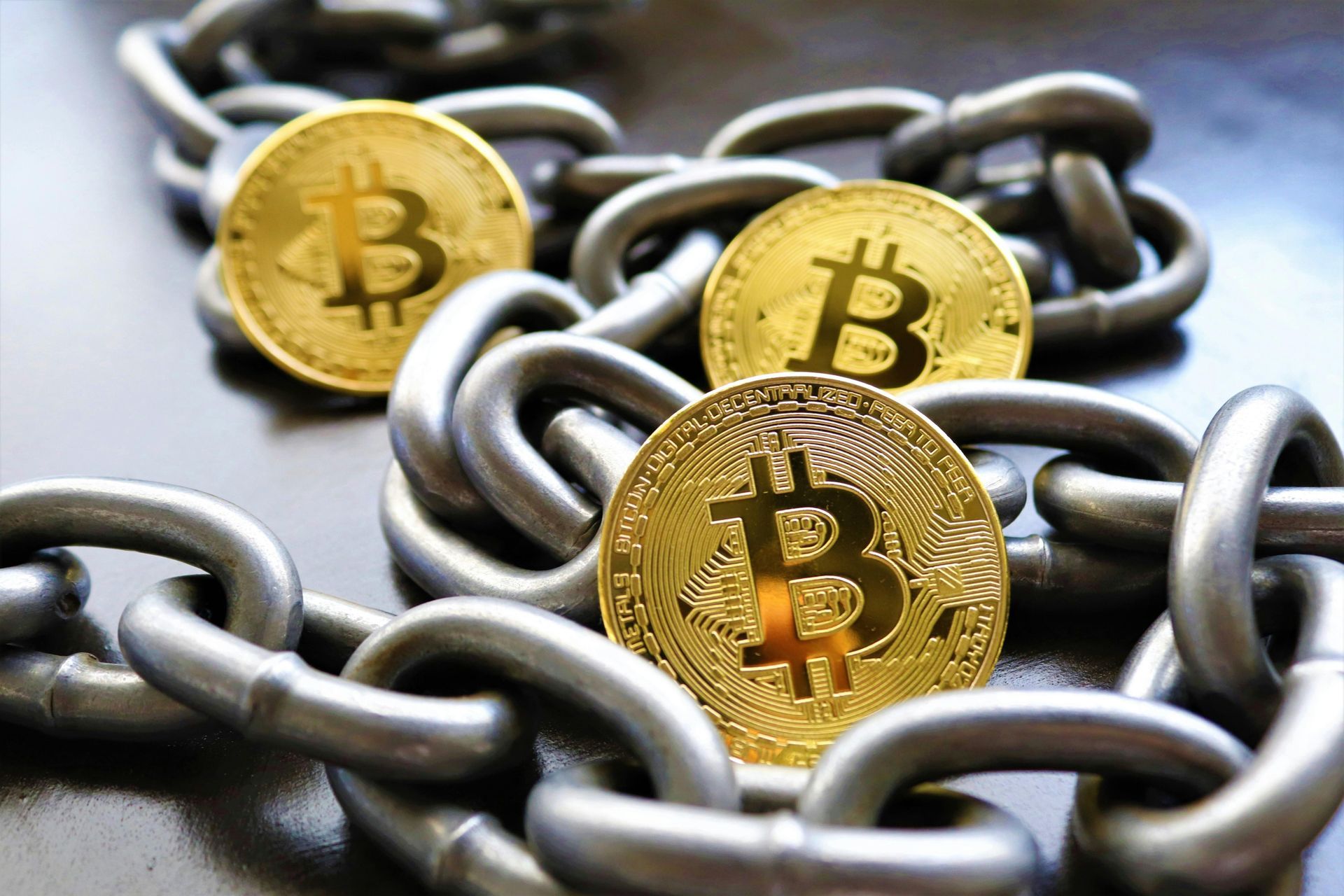 Golden Bitcoin coins nested in a heavy steel chain.