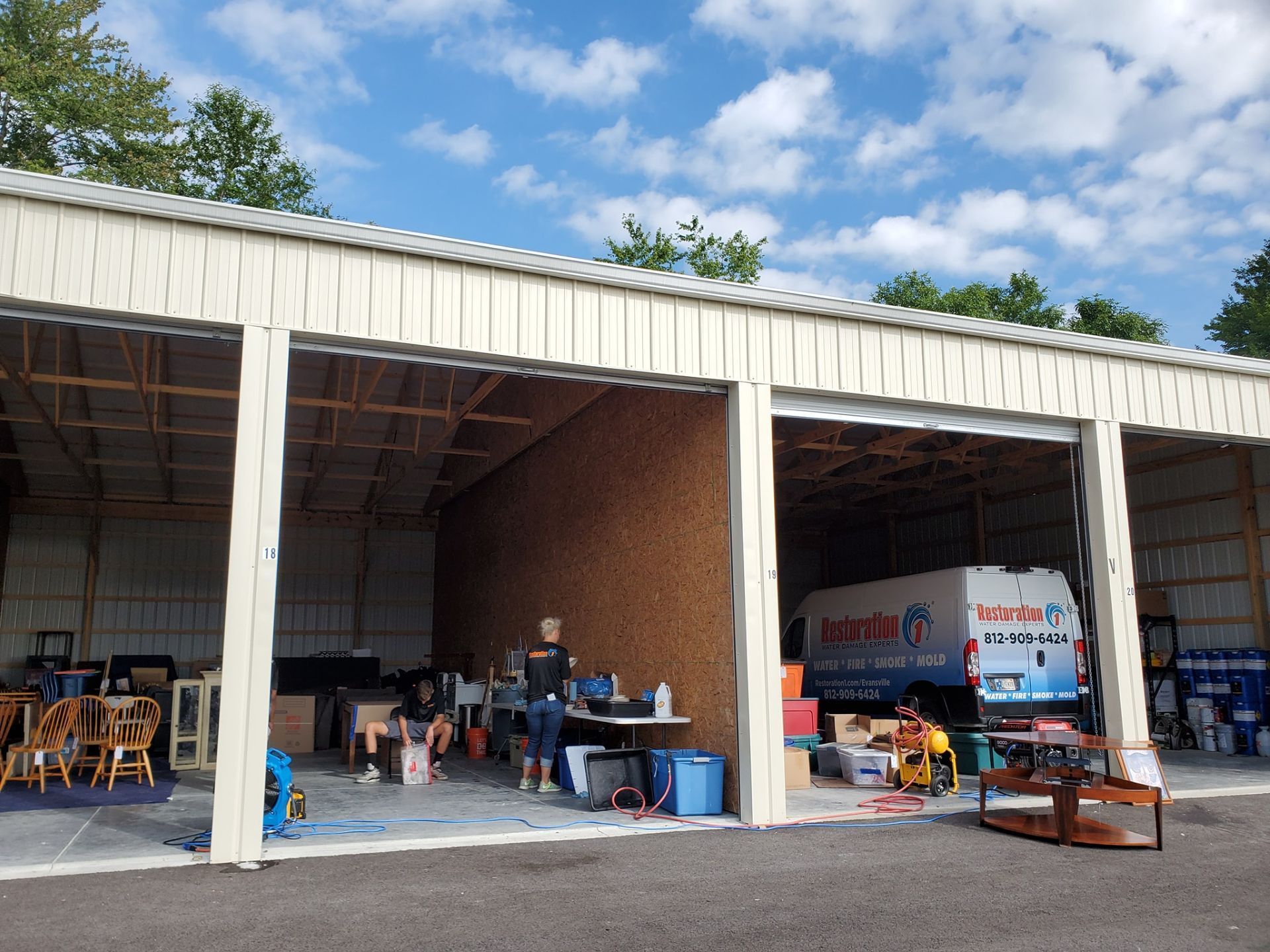 A side-by-side storage shed under a blue sky, with people working inside and an ice cream van parked in the right bay.