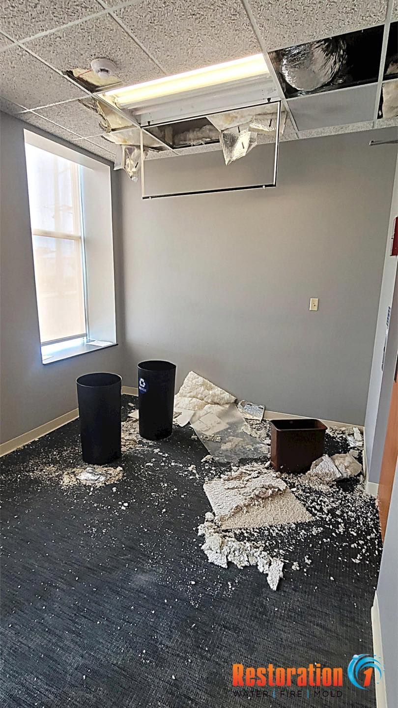 Office interior with a damaged ceiling, scattered debris on the carpet, and trash bins catching water from a leak.