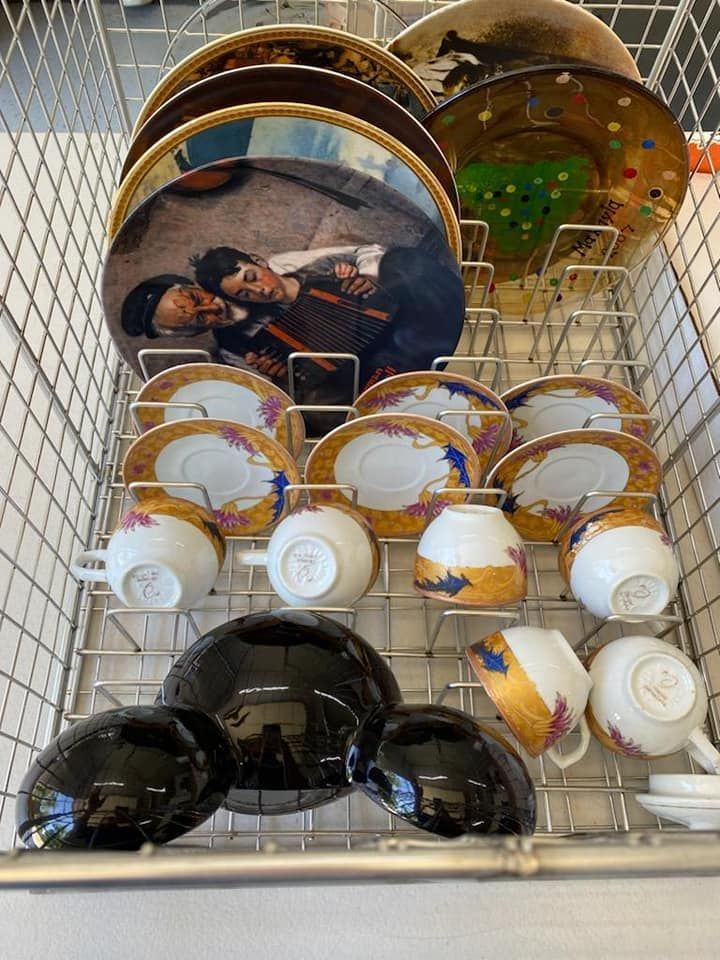 A dishwasher rack holding several decorated plates, saucers, teacups, and three black bowls.