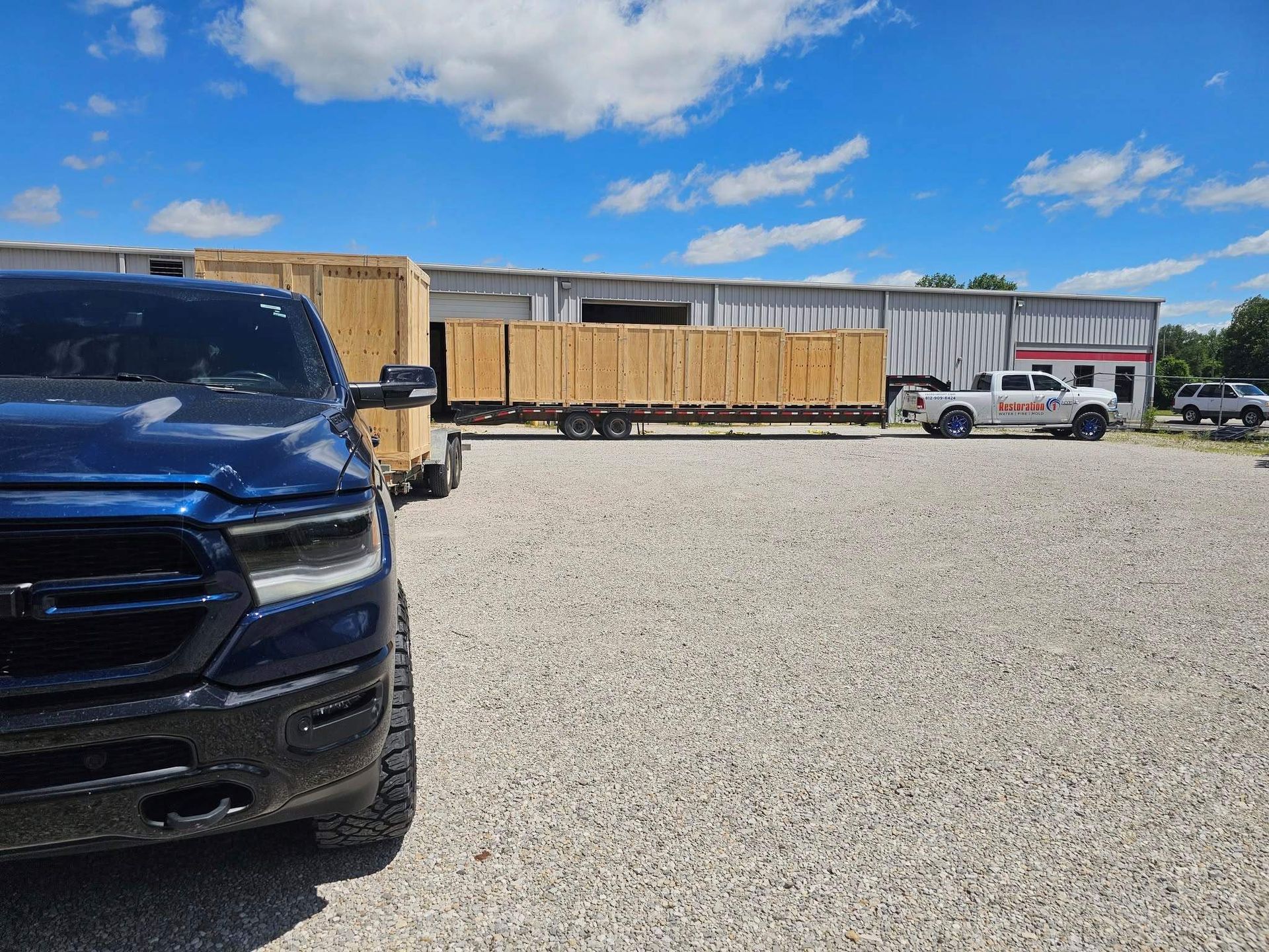 A blue pickup truck sits in a gravel lot next to a trailer loaded with several large wooden shipping crates.