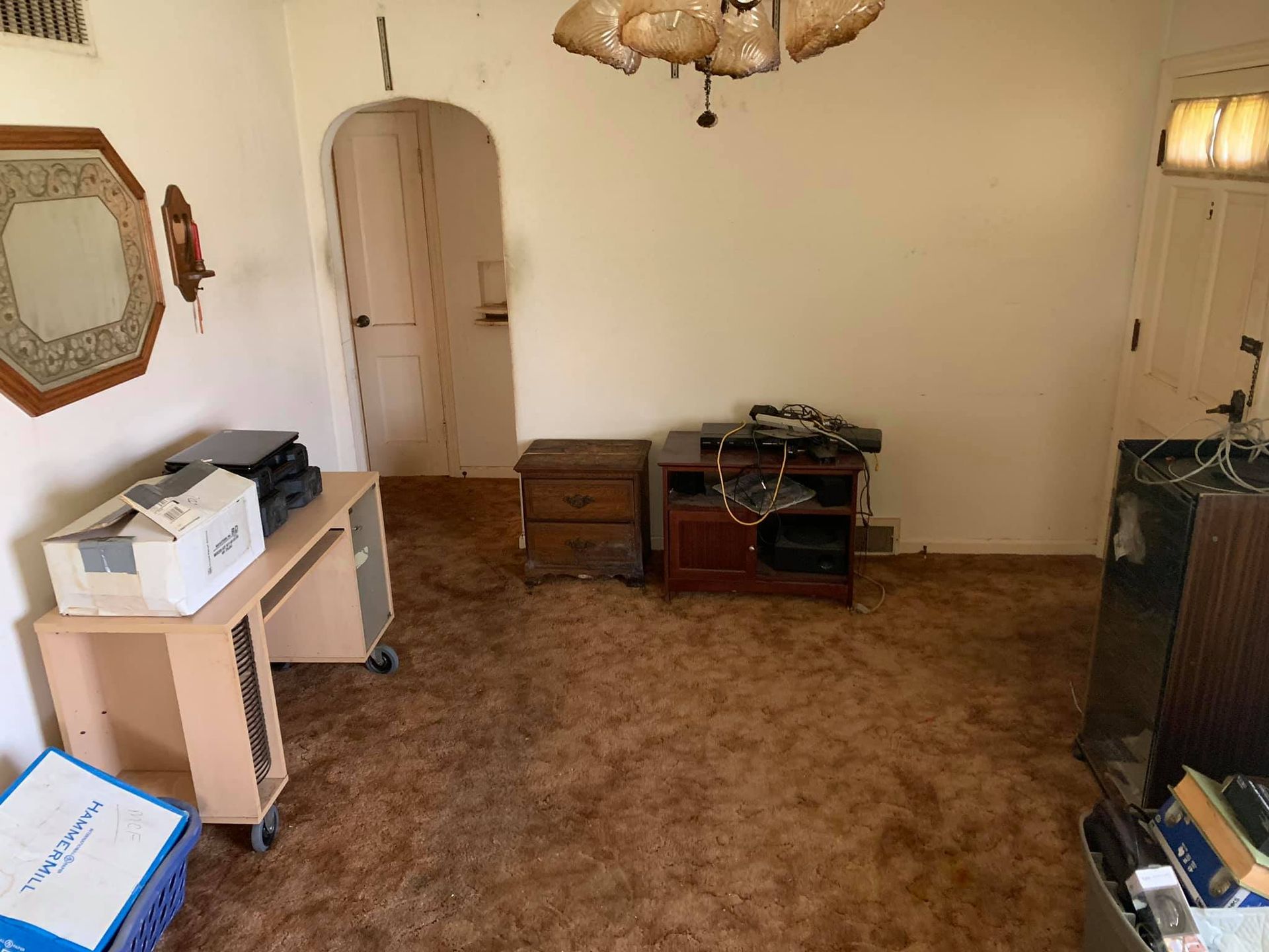 A sparse, dated room with brown shag carpet, a light-wood desk, a brown wooden side table, a dark wood media console, and a door.