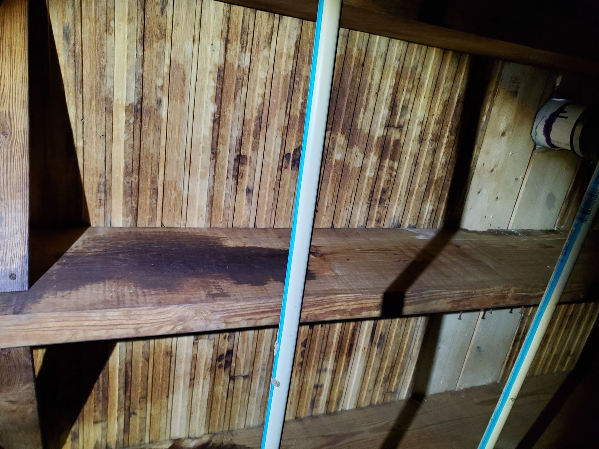 Wood shelving in a dark, unfinished space shows a prominent dark moisture stain on the middle shelf.