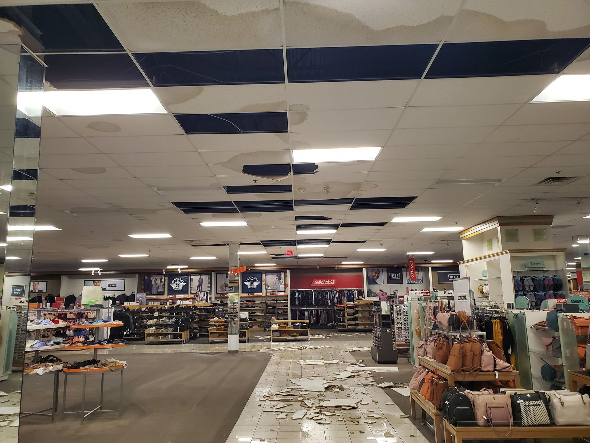 Interior of a retail store with multiple missing ceiling tiles and debris scattered across the floor.