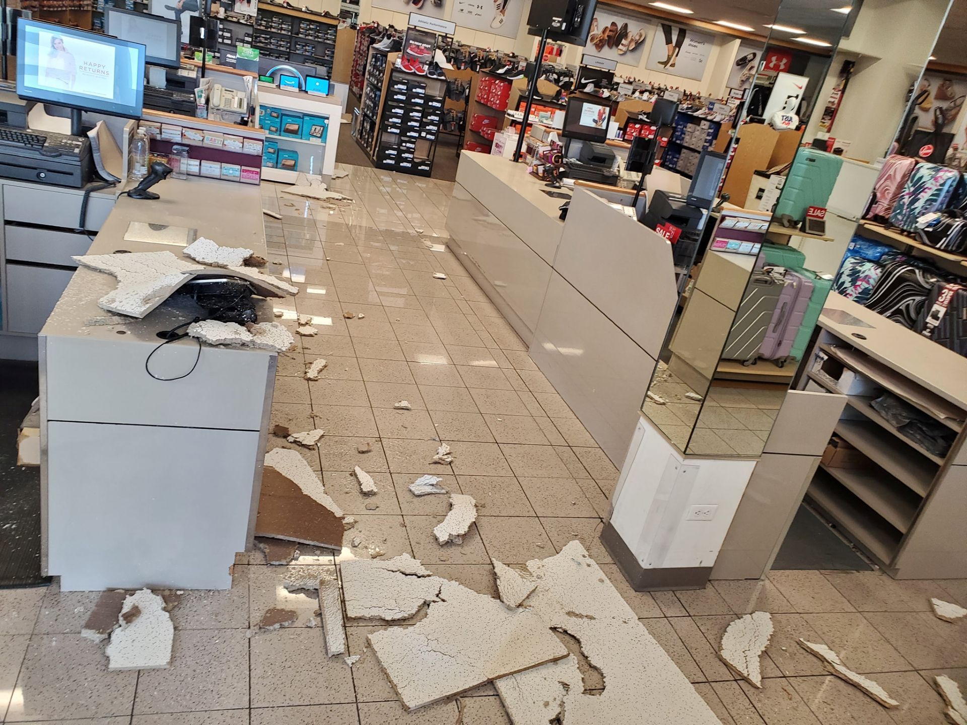 A retail store checkout counter with debris scattered across the floor from a fallen ceiling panel.