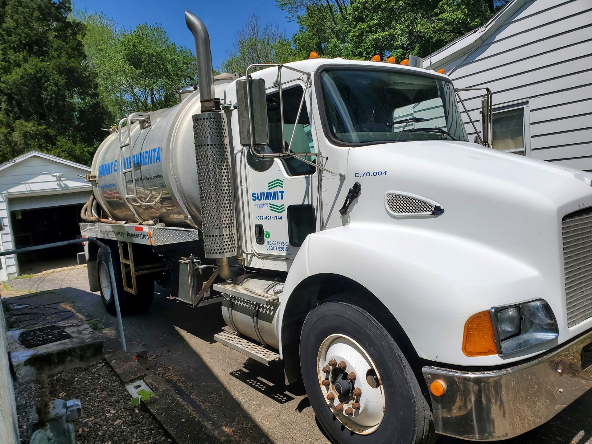 A white septic vacuum truck parked on a residential driveway next to a small white garage.