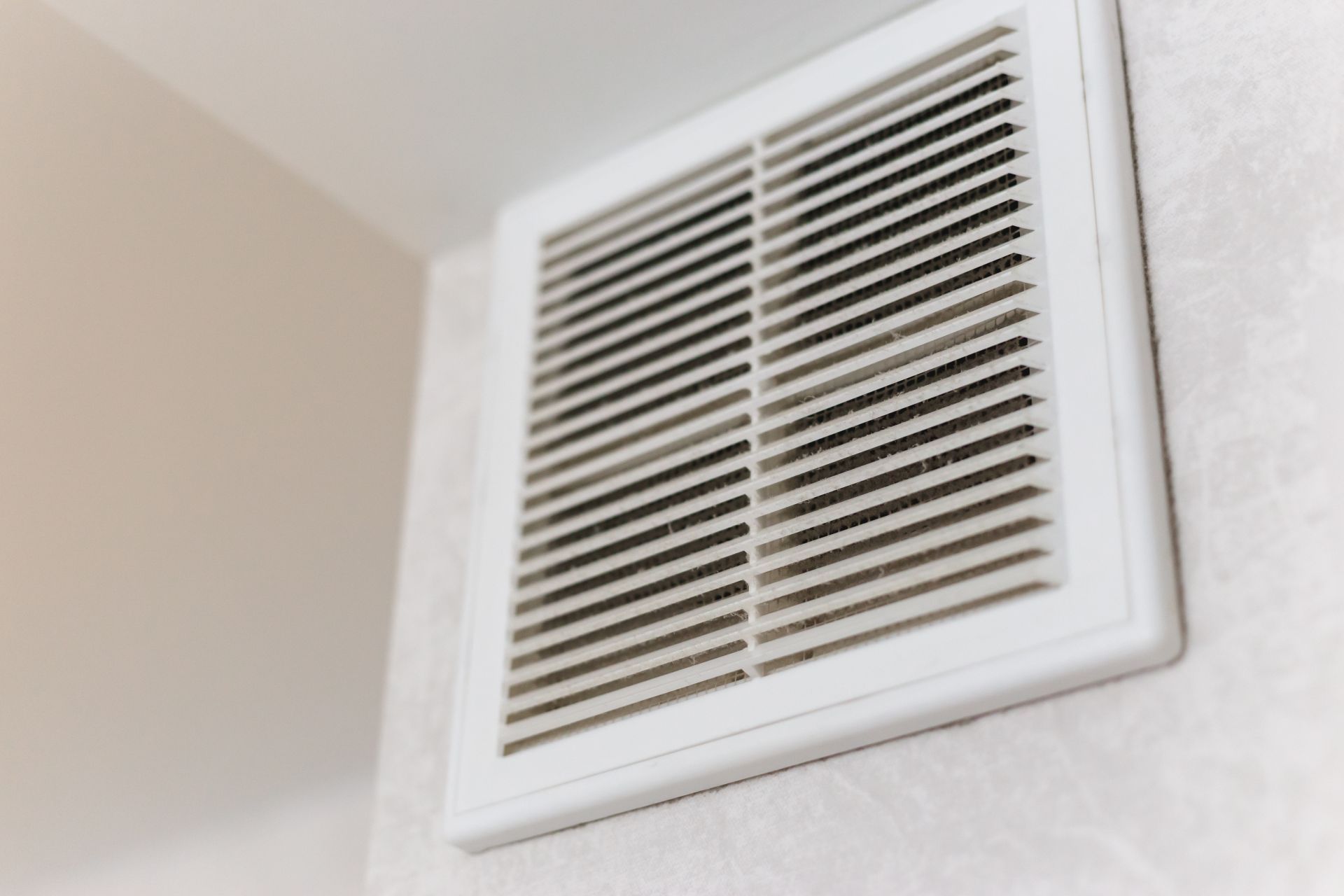 A white rectangular ventilation grille mounted on a light-colored wall.