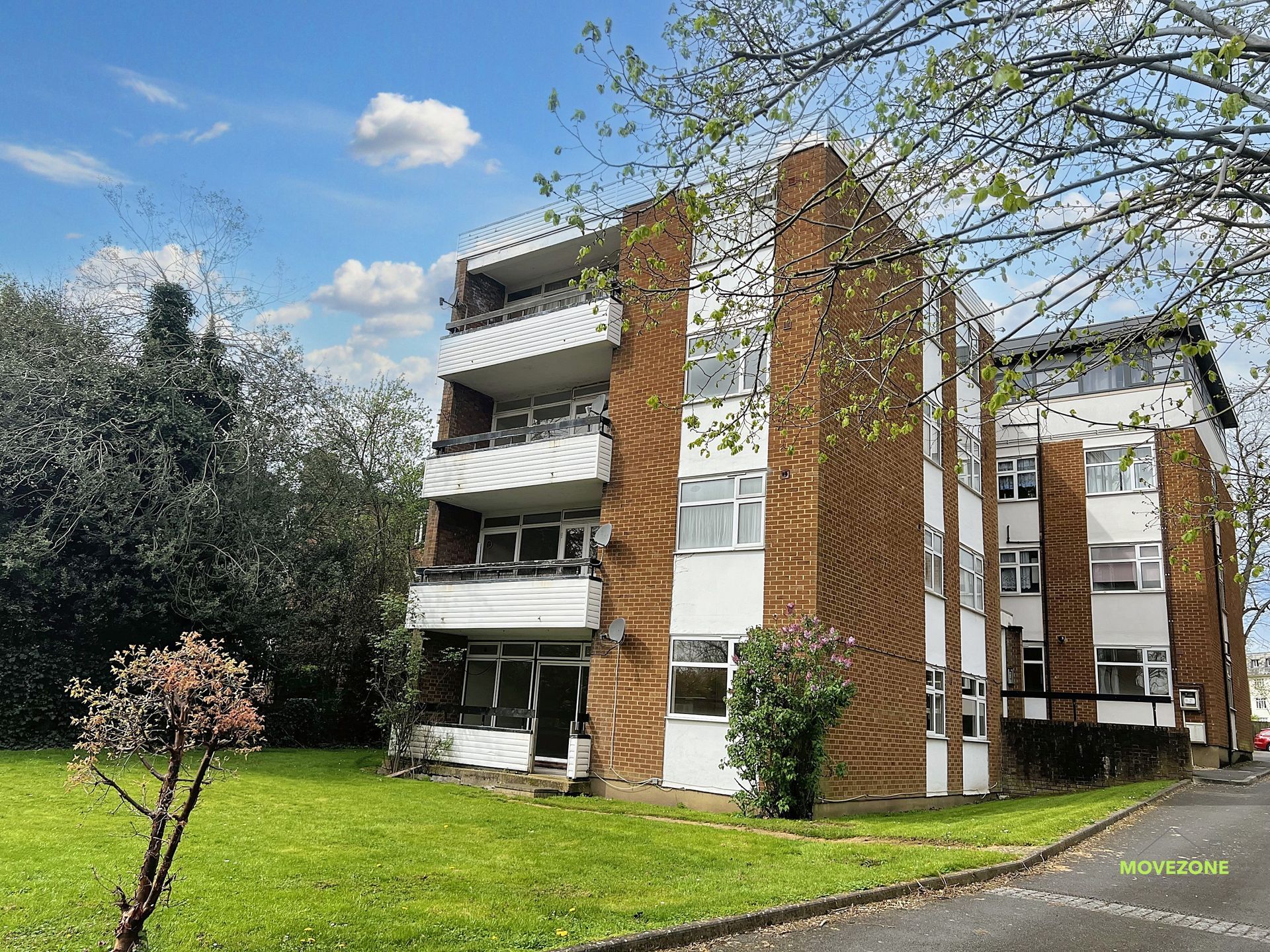 Apartment building with balconies beside a green lawn and trees under a blue sky