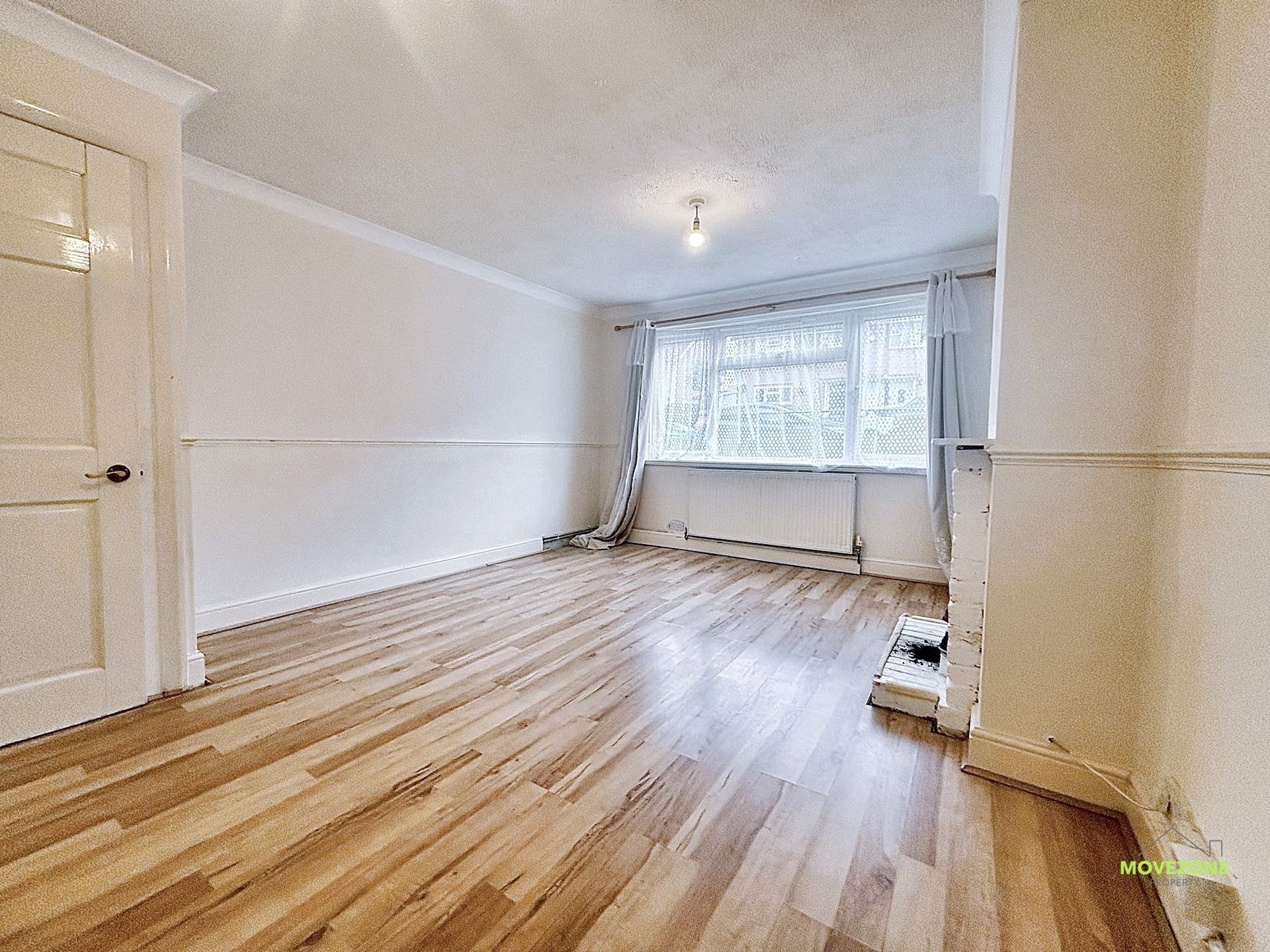 Empty white room with wood floor, window and radiator, viewed from the doorway