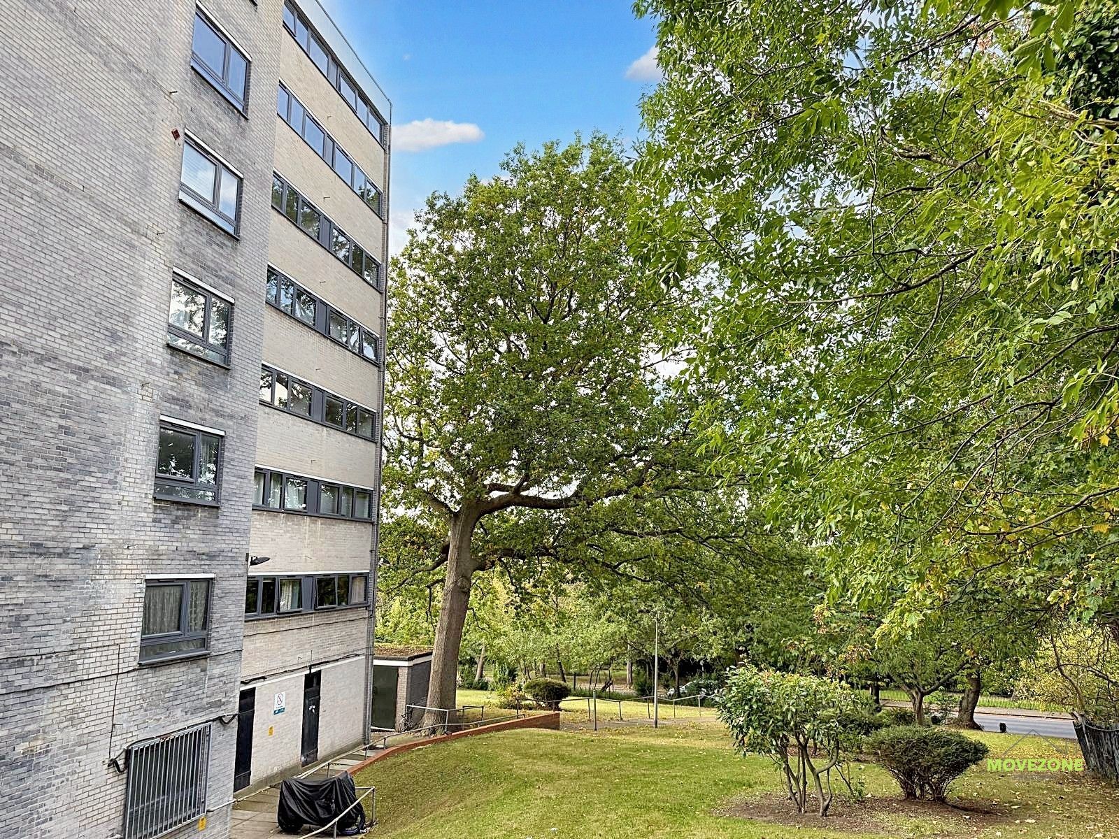 Apartment building beside a grassy courtyard with large trees and a blue sky
