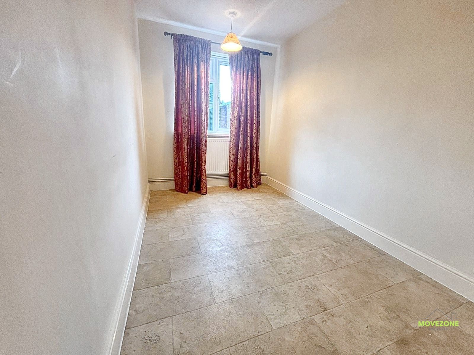 Empty narrow room with tiled floor, white walls, and a window with curtains at the far end.