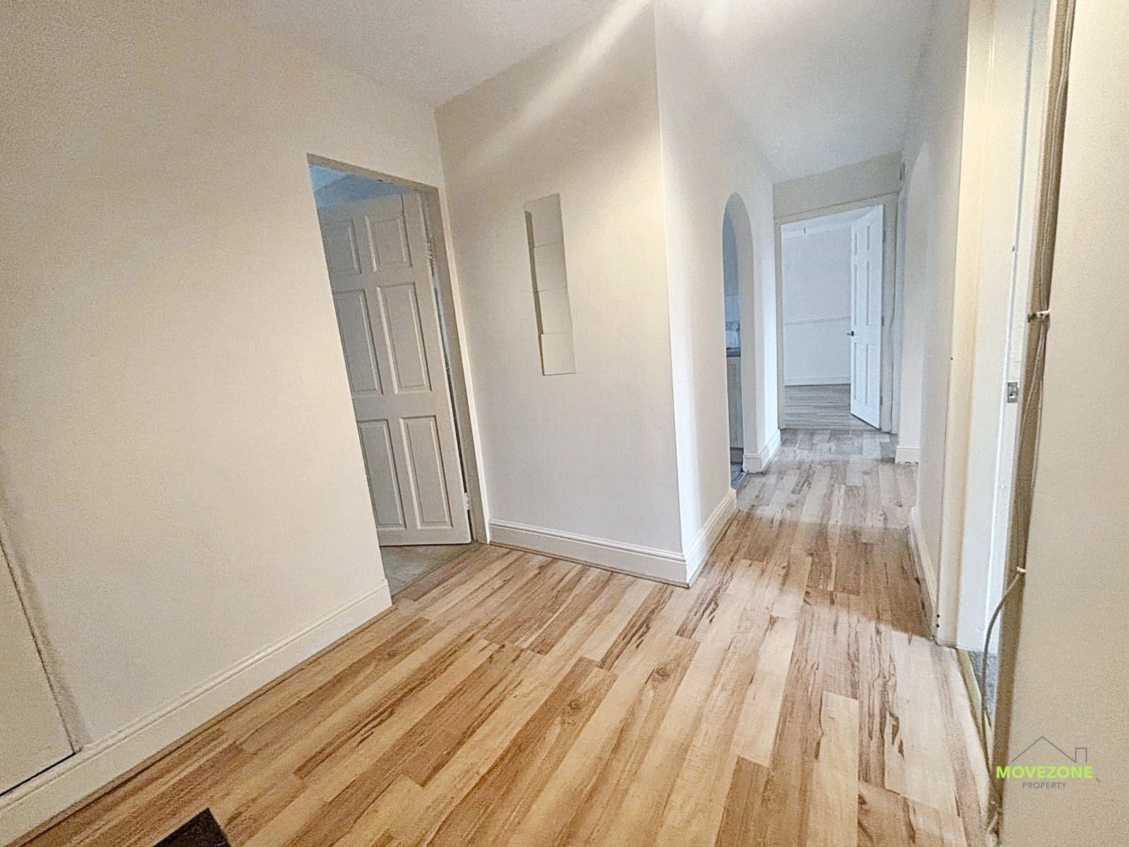 Empty hallway with white walls, wood floors, and several doorways leading to rooms