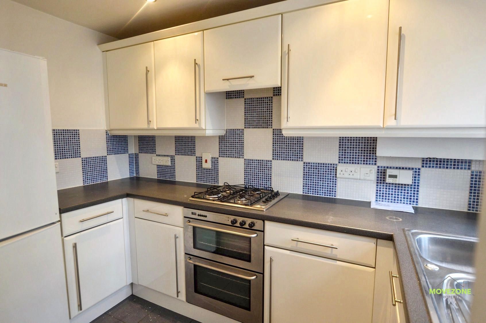 Compact white kitchen with blue checkered tile backsplash, stove, oven, cabinets, and sink