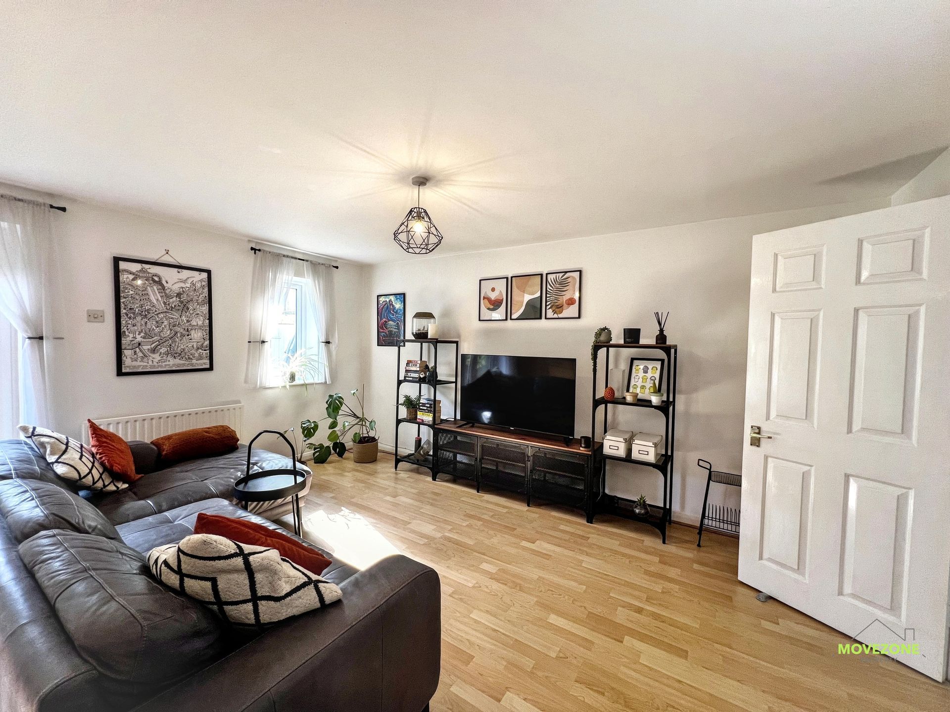Bright living room with leather sofas, TV stand, wall art, and wood flooring