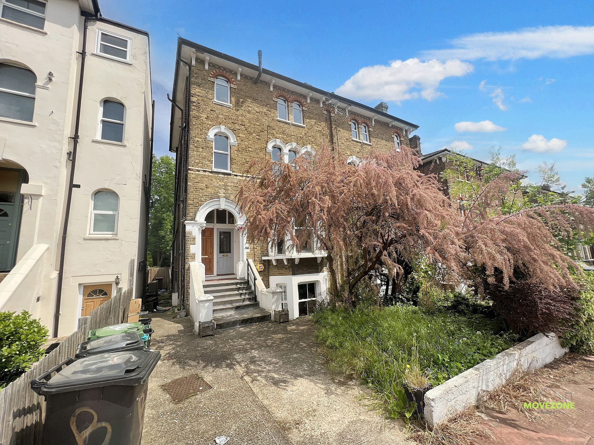 Brick townhouse with white steps and overgrown flowering tree in a small courtyard