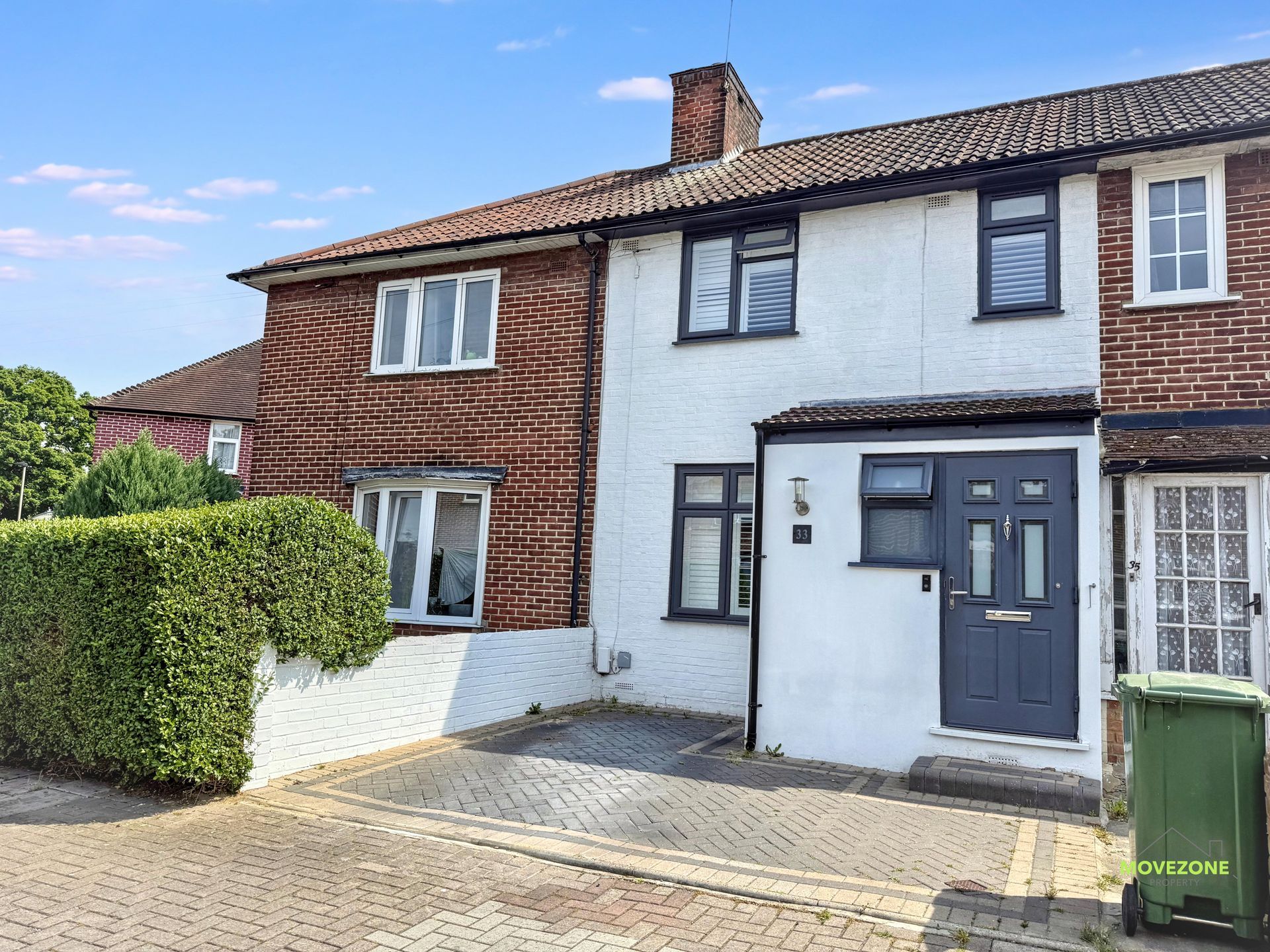 Semi-detached brick house with white facade, dark front door, hedge, and paved driveway