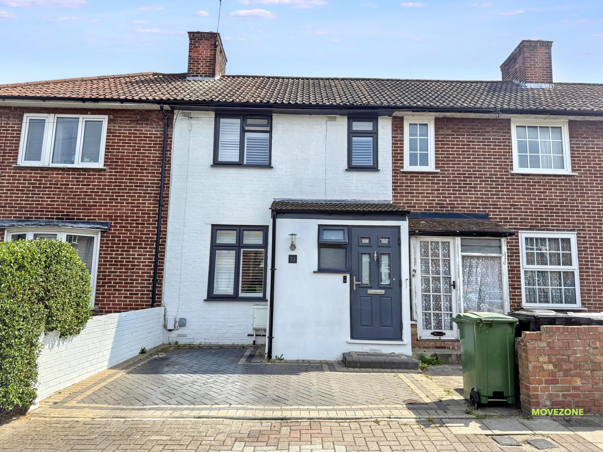 Front view of a red-brick terraced house with a gray front door and paved driveway