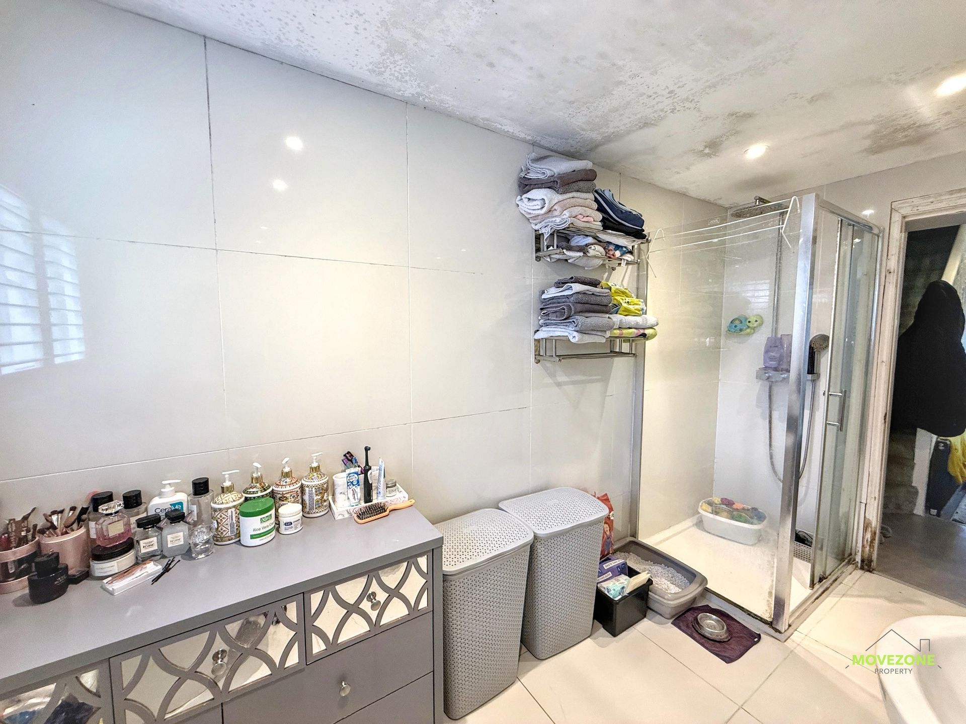 Small bathroom with sink, toiletries on a shelf, a trash bin, and a shower curtain by the tub.