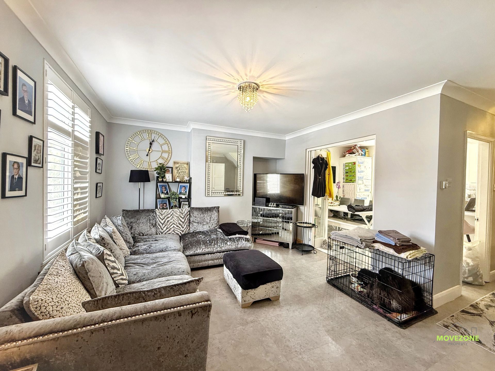 Bright living room with gray sectional, TV, black ottoman, and pet crate by a doorway.