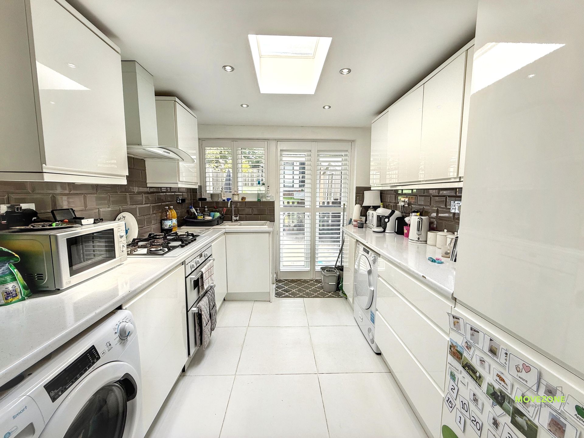 Bright white galley kitchen with skylight, white cabinets, washer, and glass doors at the end.
