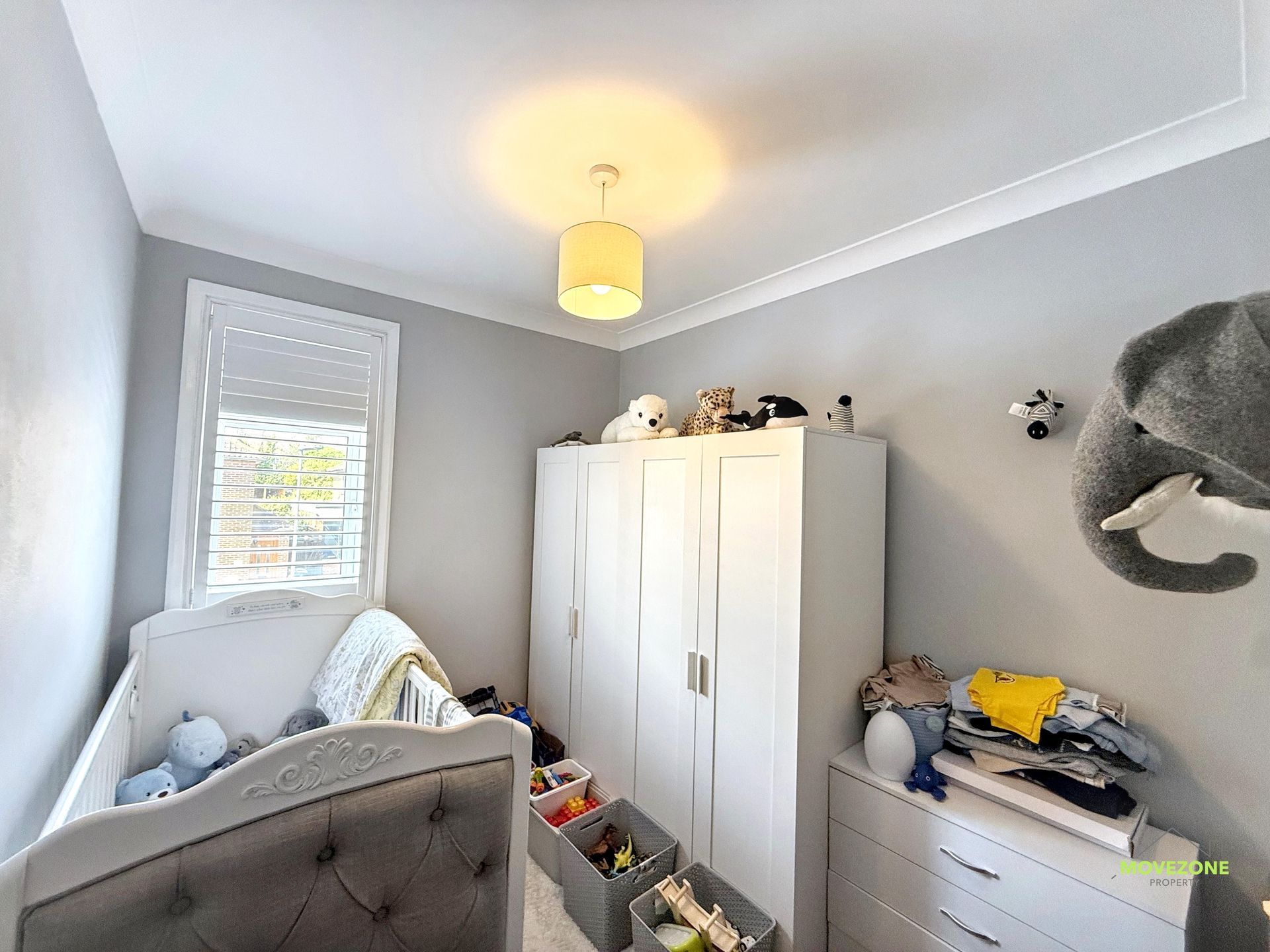 A small gray-and-white bedroom with a white wardrobe, crib, toy storage, and an elephant wall decoration.