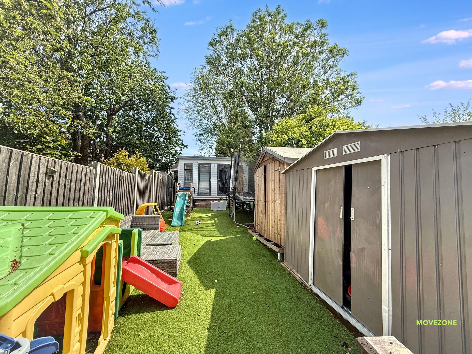 Backyard with a playset, turf lawn, and tan storage shed beside a wooden fence.