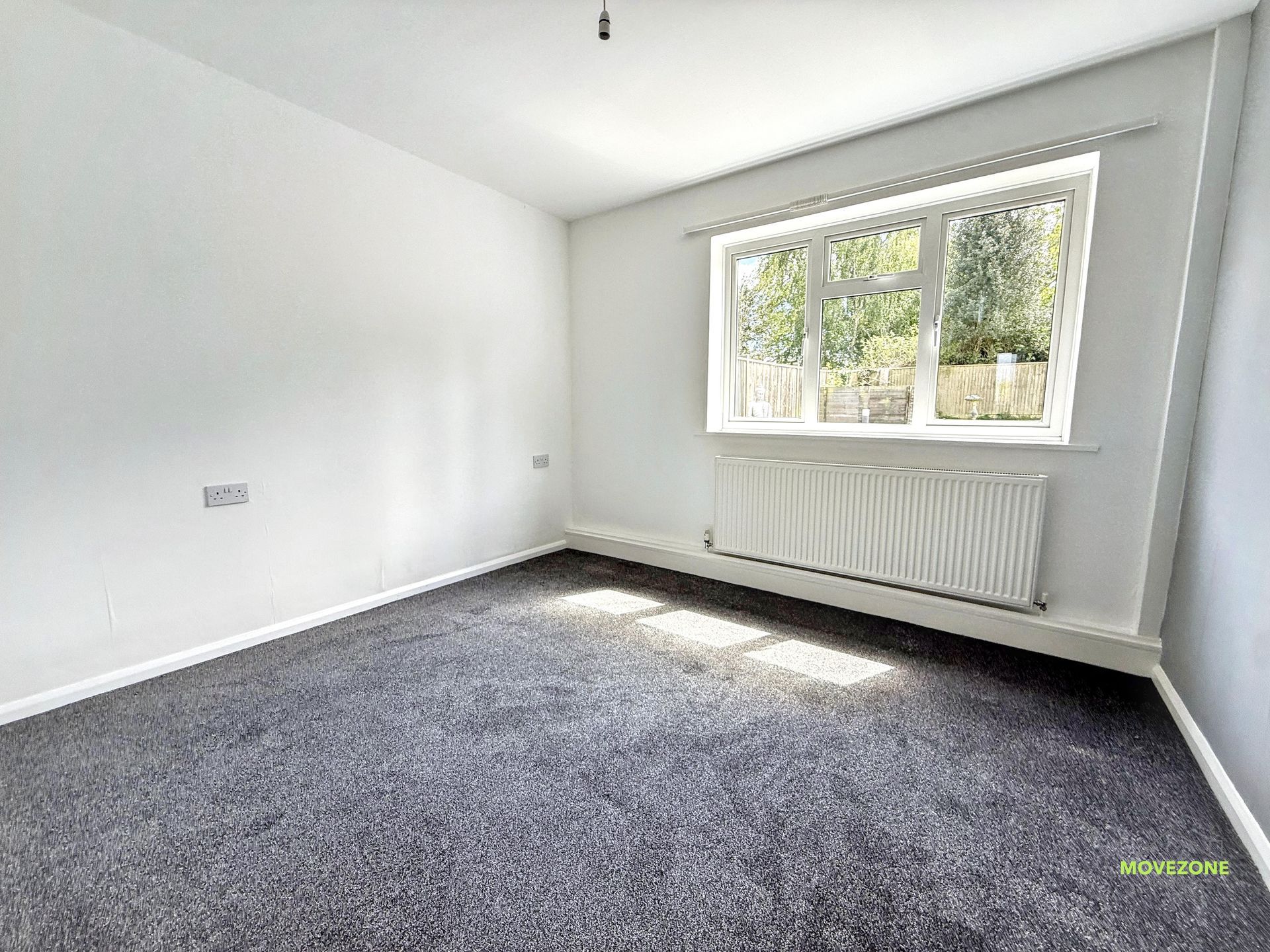 Empty white room with gray carpet, window, and radiator on the far wall.