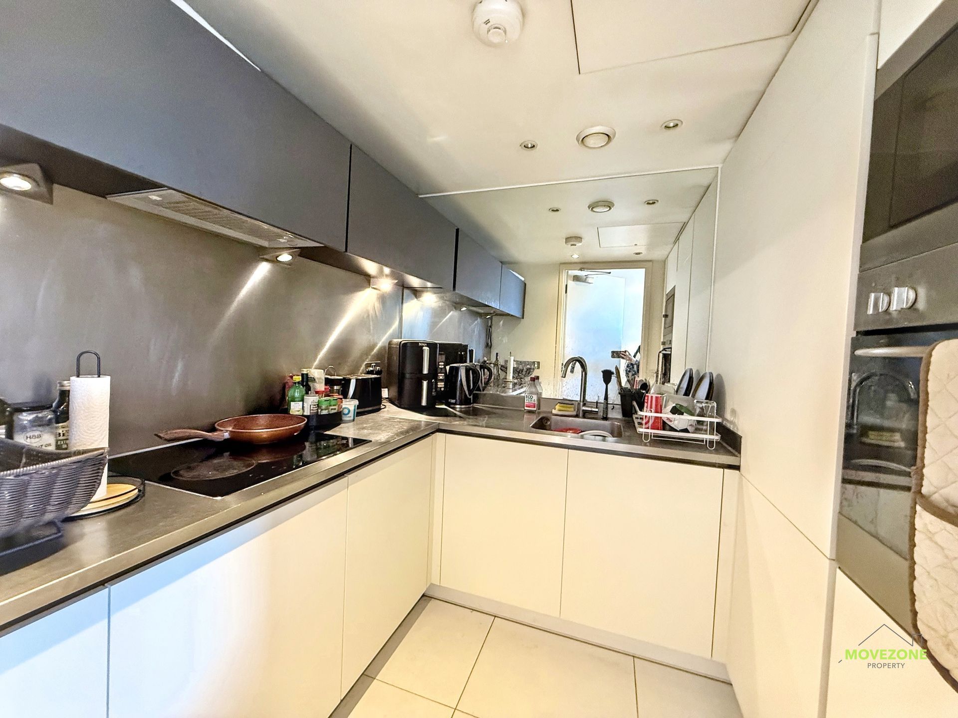 Modern narrow kitchen with white cabinets, black countertops, stainless appliances, and a window at the end.