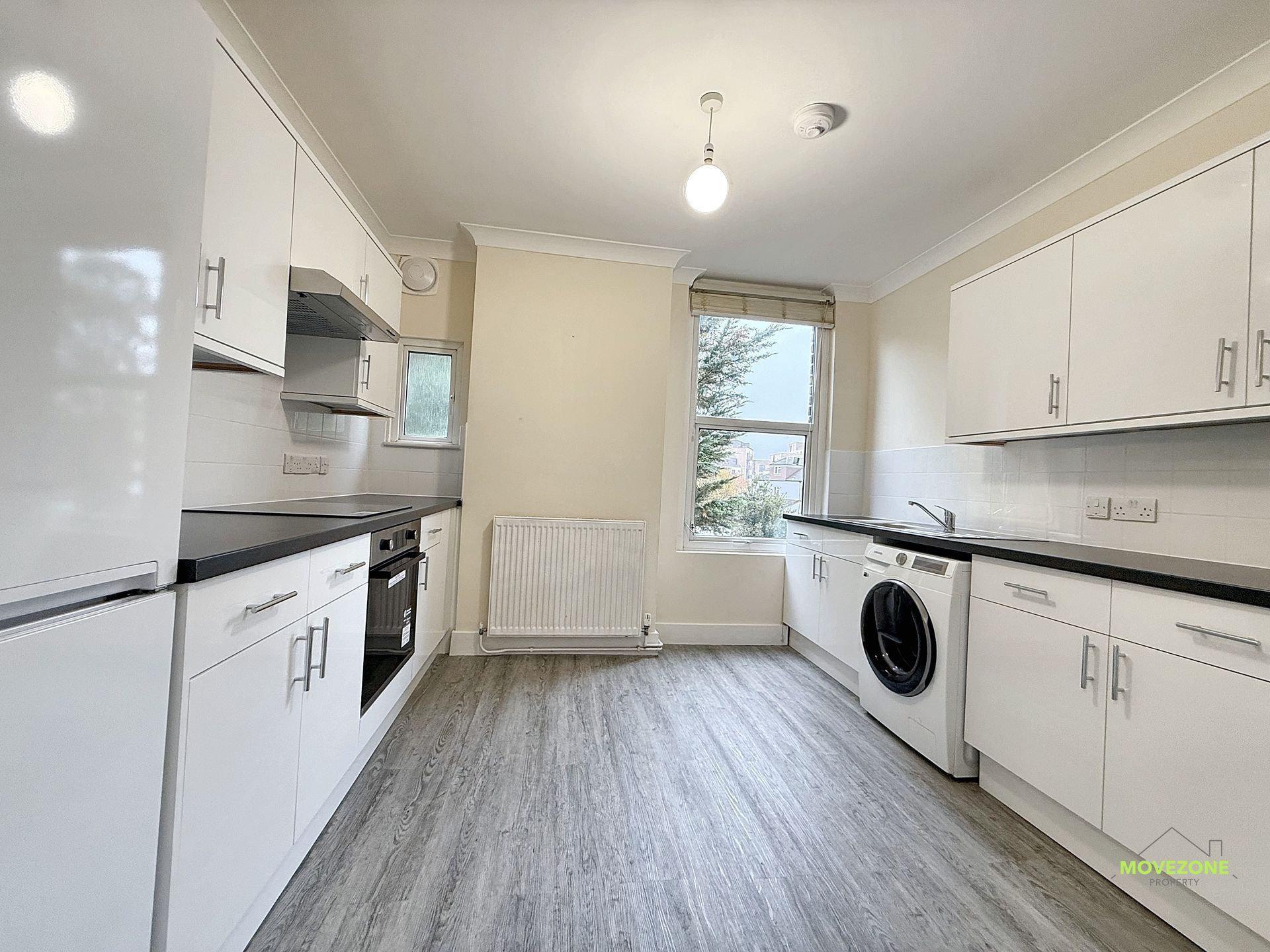 Bright white galley kitchen with black countertops, washer, and a window at the far end