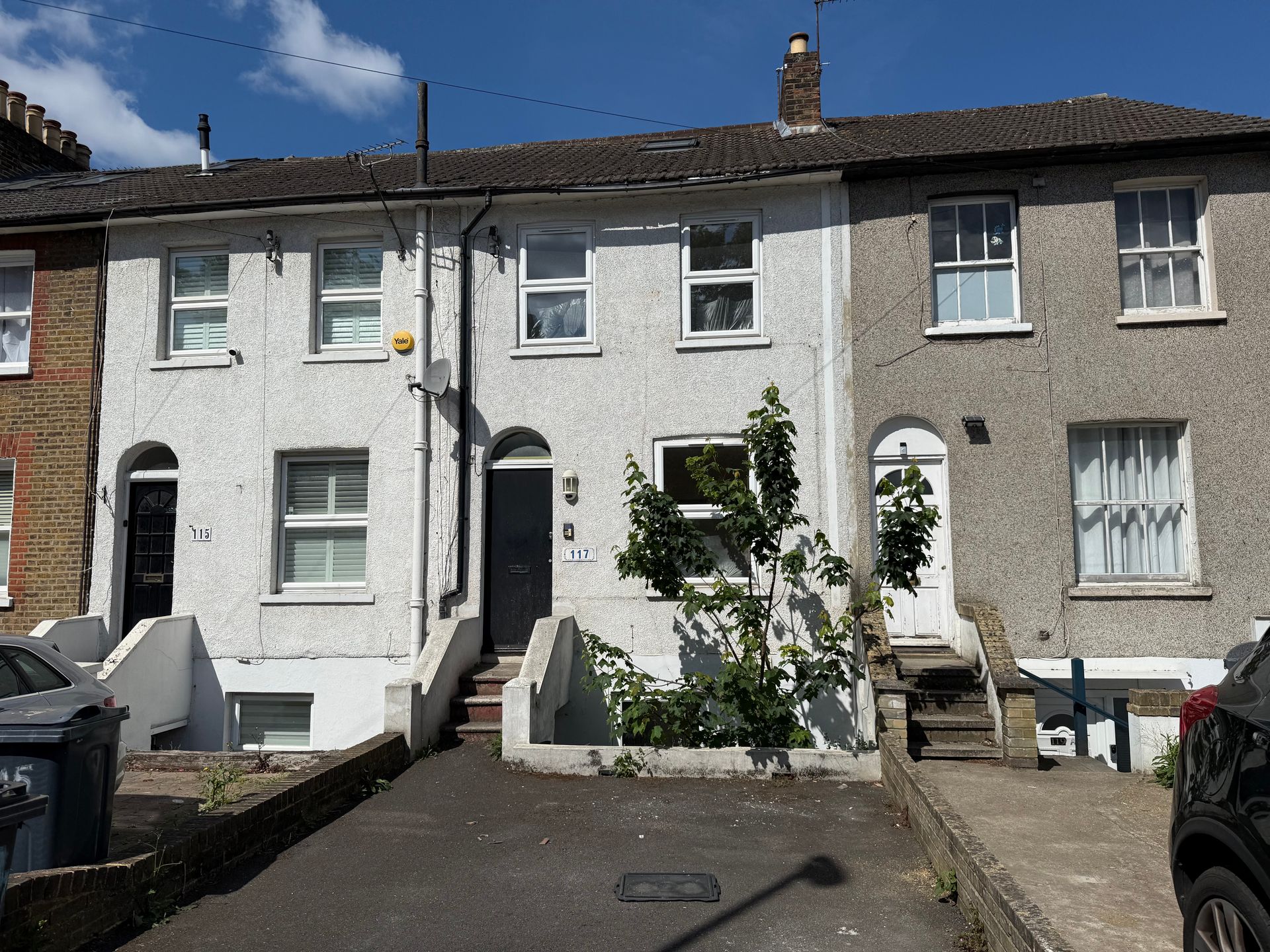 Row of small white terraced houses with front steps and a parked car on a sunny street