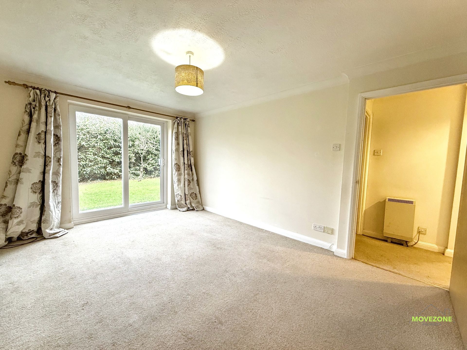 Empty beige living room with sliding glass doors, curtains, and an open doorway to a bathroom